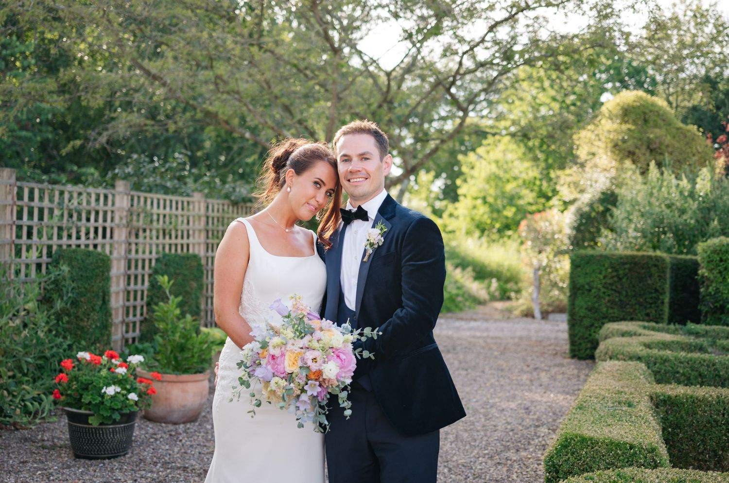 Newlyweds walking together through a formal garden pathway.