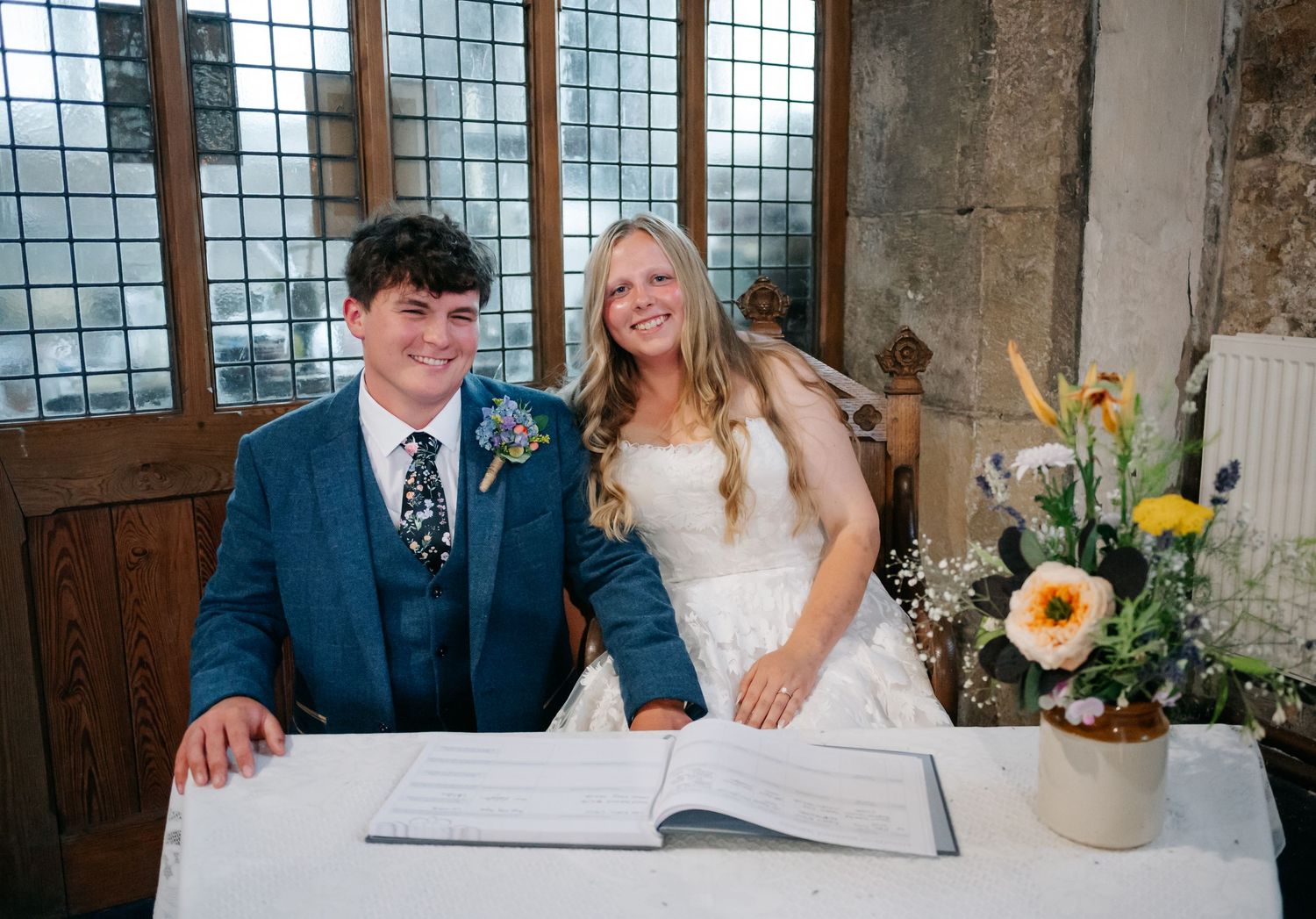 Couple signs marriage register at church altar with stained glass windows in background.