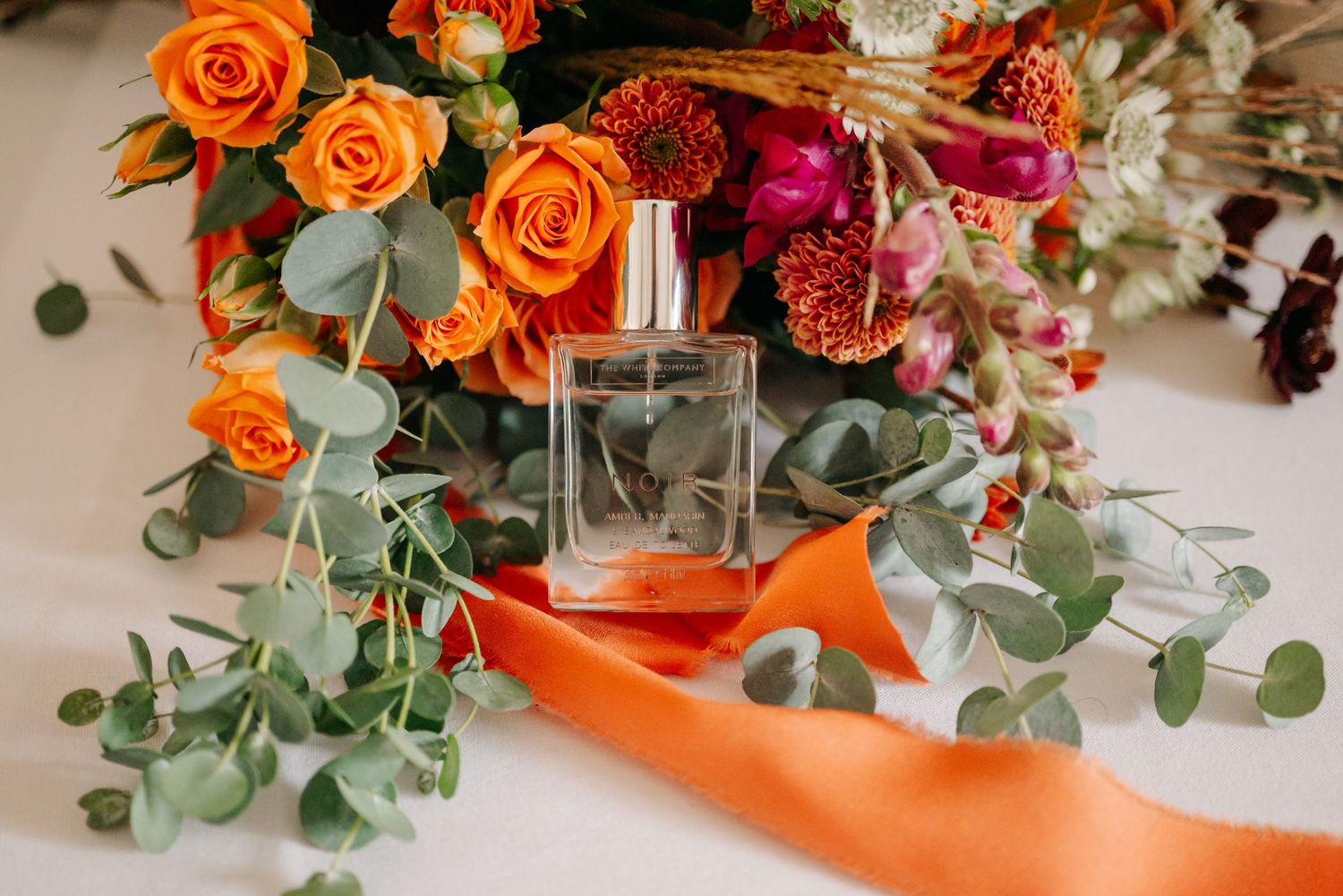 Orange roses and burgundy flowers arranged with eucalyptus greenery in a romantic wedding centerpiece display.