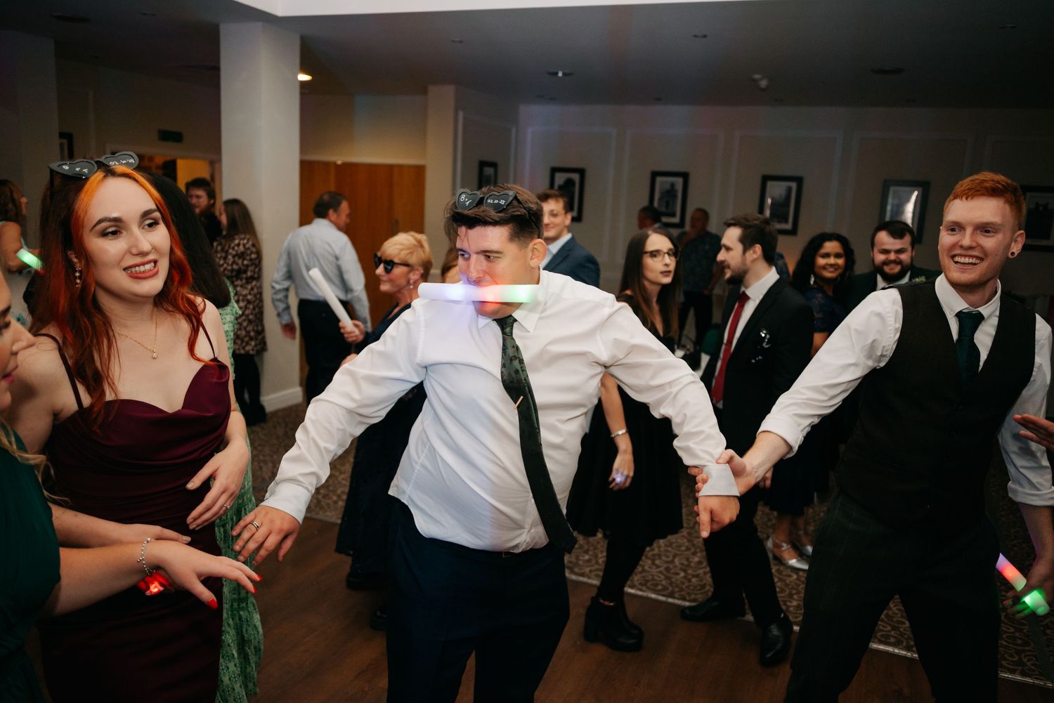 Wedding reception guests dancing and celebrating in a dimly lit venue.