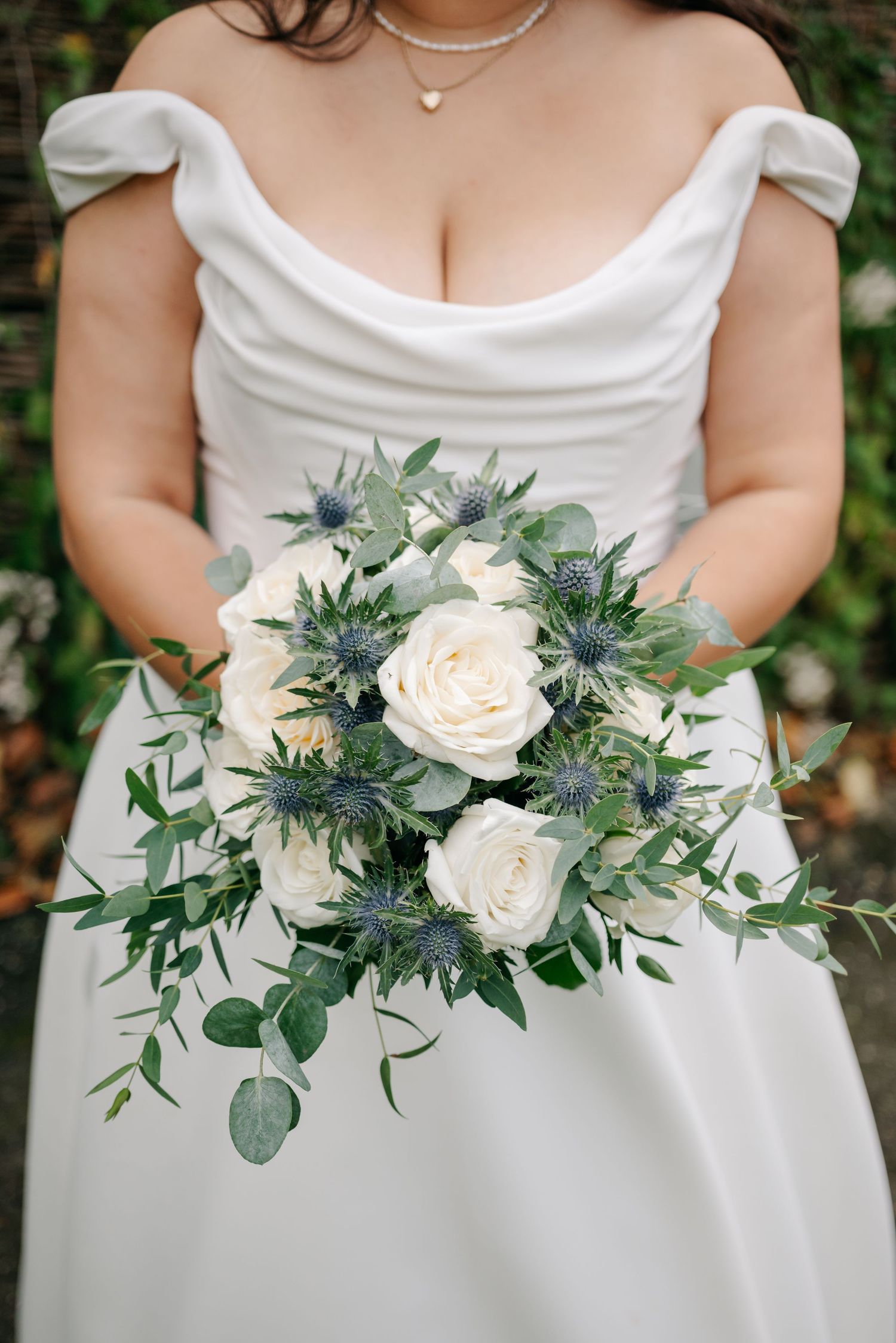 Elegant white and green wedding bouquets with roses and eucalyptus leaves held against white dresses.
