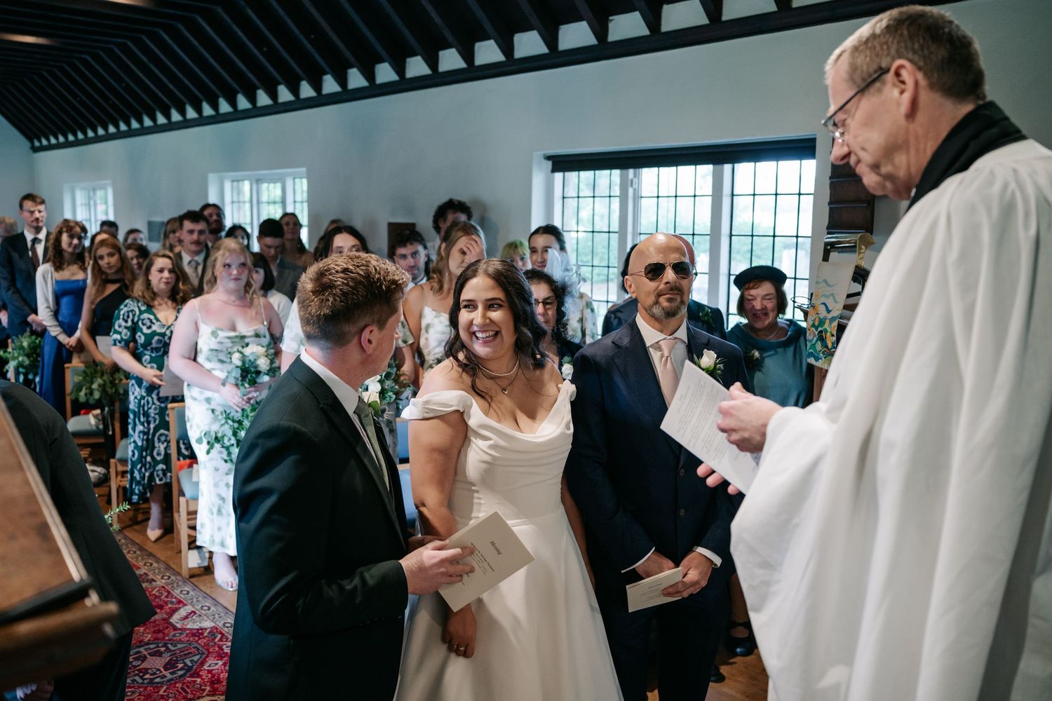 A wedding celebration scene showing guests gathered in a bright indoor venue during a ceremony.