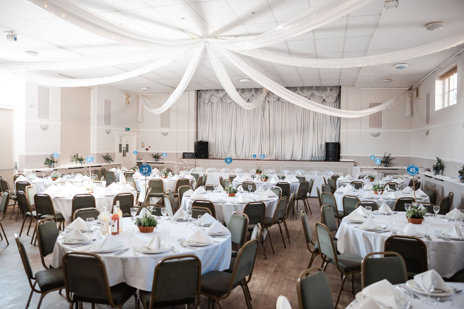 White banquet hall decorated with draped fabric and round tables set for an elegant wedding reception.