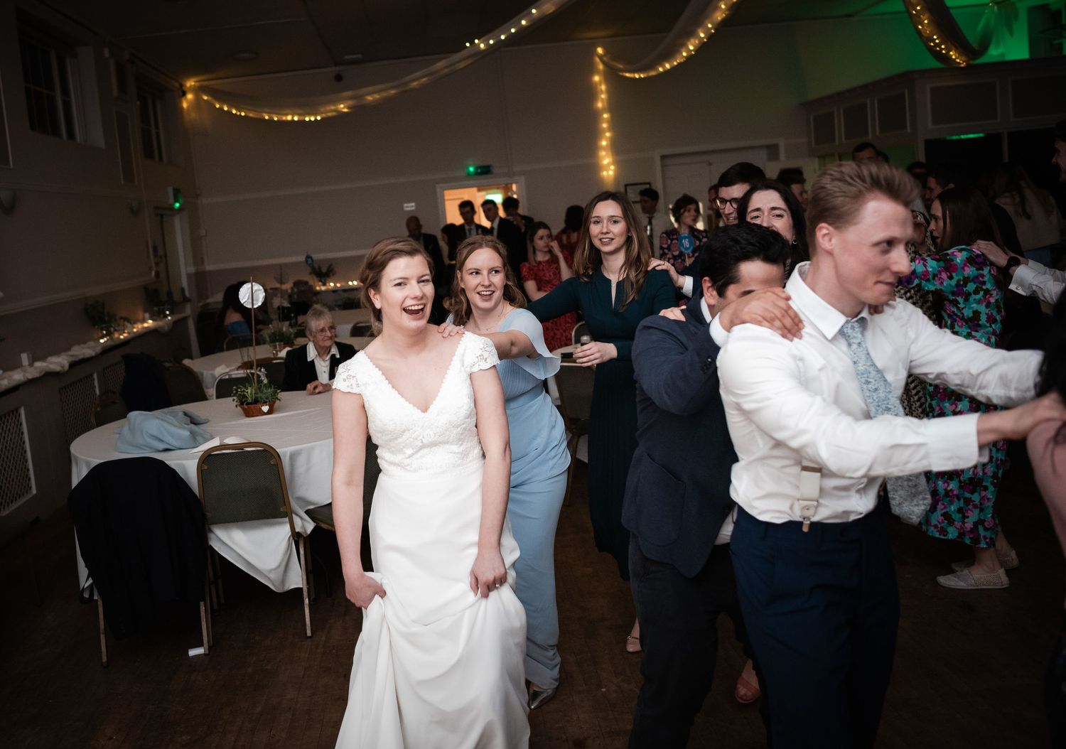 Wedding reception dance party with string lights and guests celebrating.
