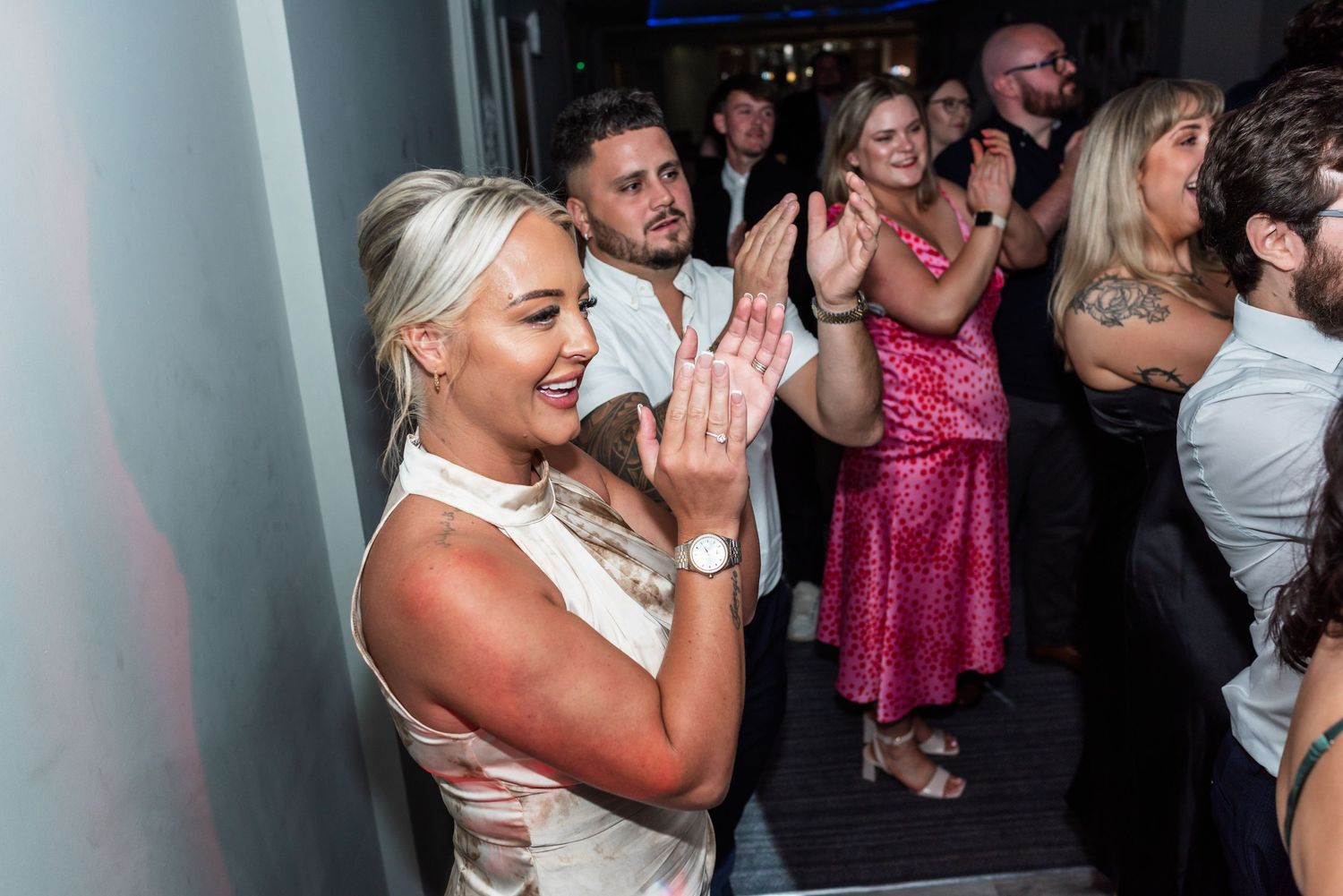 Wedding celebration on dance floor with guests dancing and clapping in evening party atmosphere.
