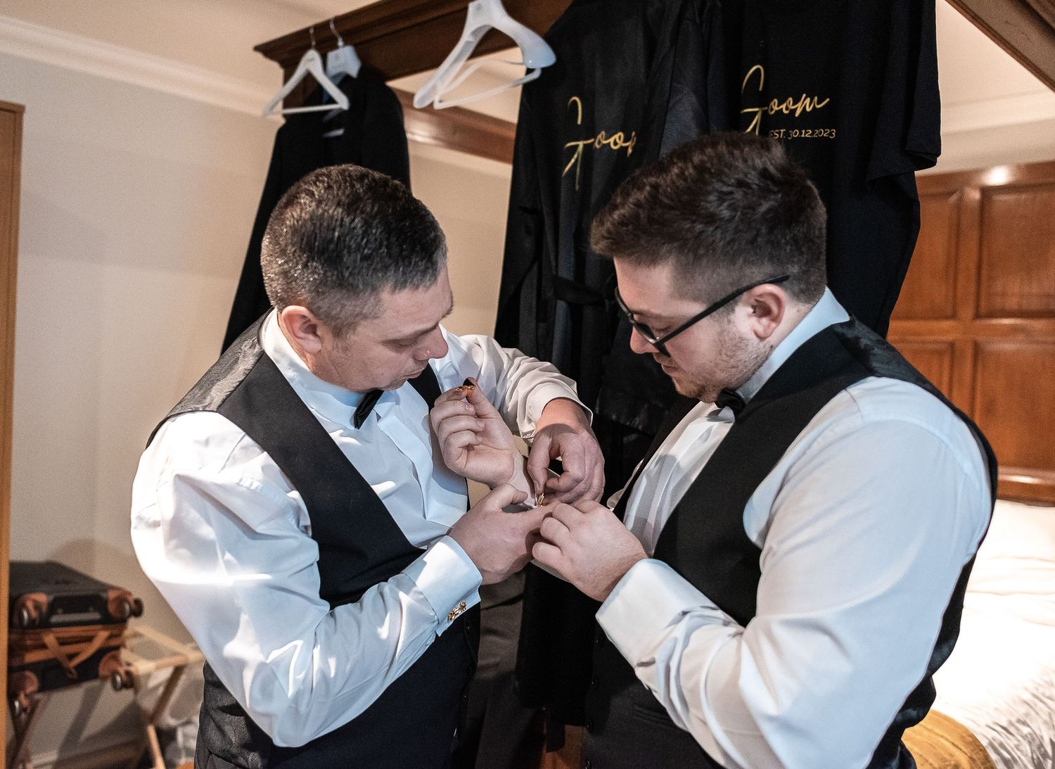 Two people in white dress shirts helping each other with formal wear accessories.