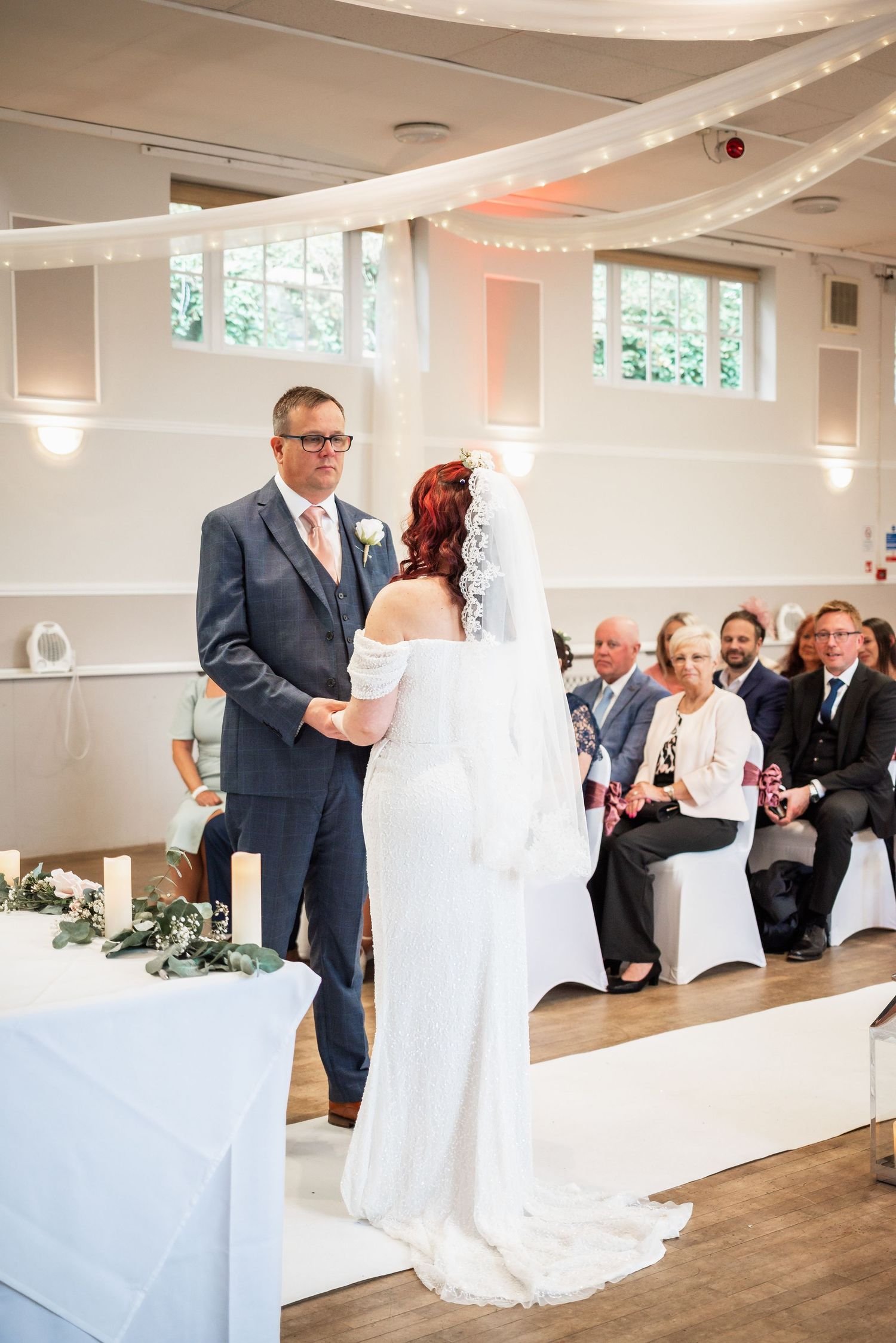 Wedding ceremony in progress in an elegant white room with draped ceiling decor.
