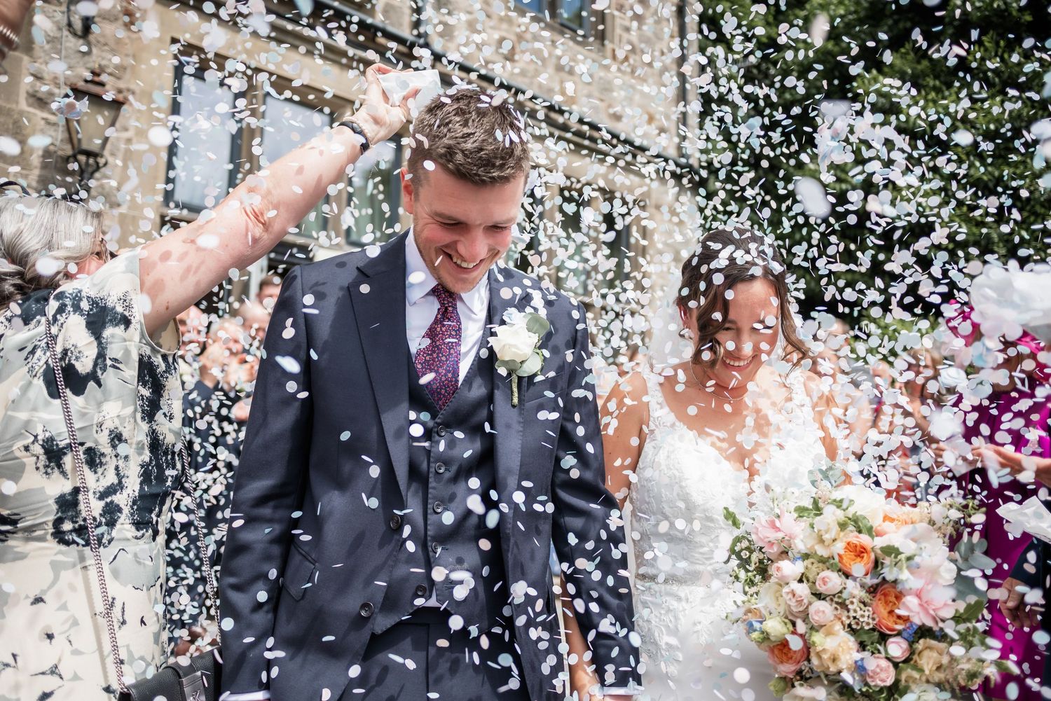 Wedding couple showered with white confetti after ceremony at stone venue.