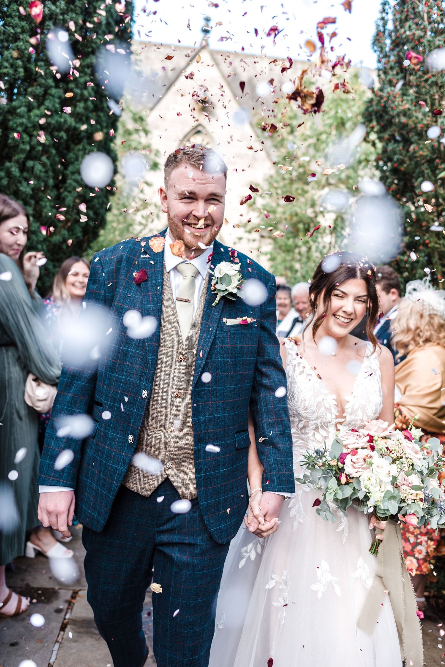 Joyful wedding celebration with confetti being thrown outside a stone chapel.