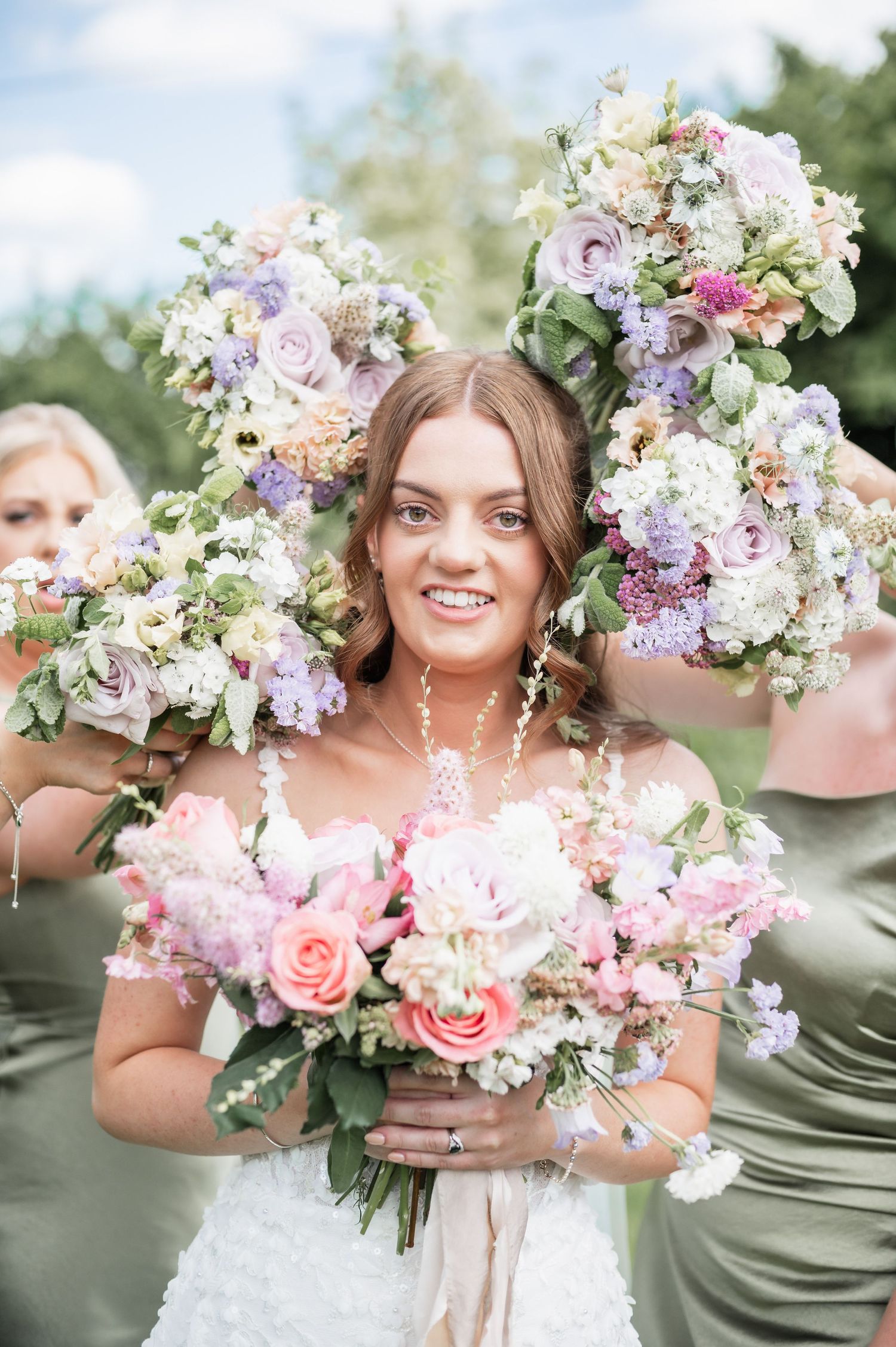 Wedding bouquets featuring soft pink and purple blooms create frame around white lace dress.