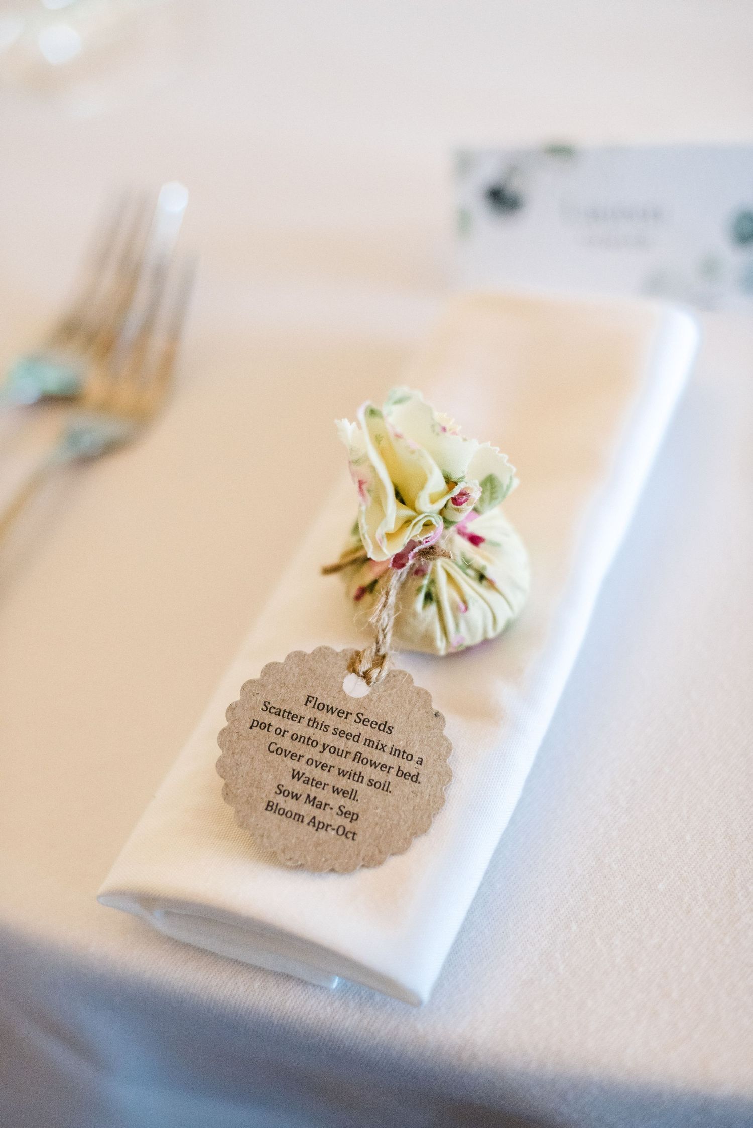 Elegant wedding place setting with folded white napkin and decorative tag on light tablecloth.