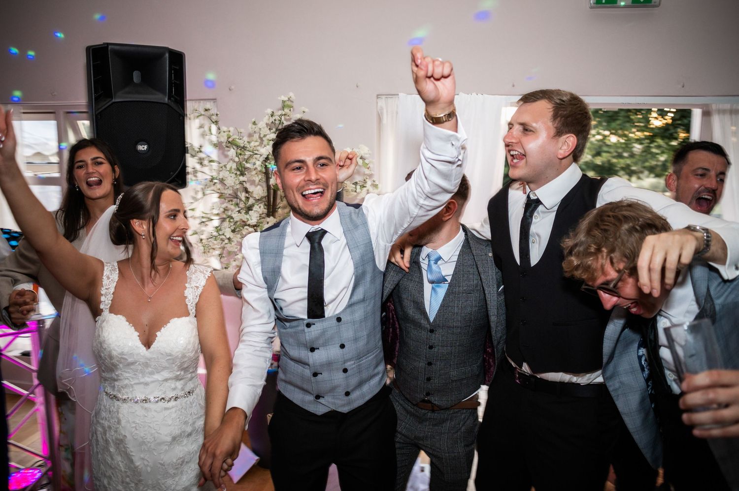 Energetic celebration scene with wedding party members dancing and cheering on the dance floor.