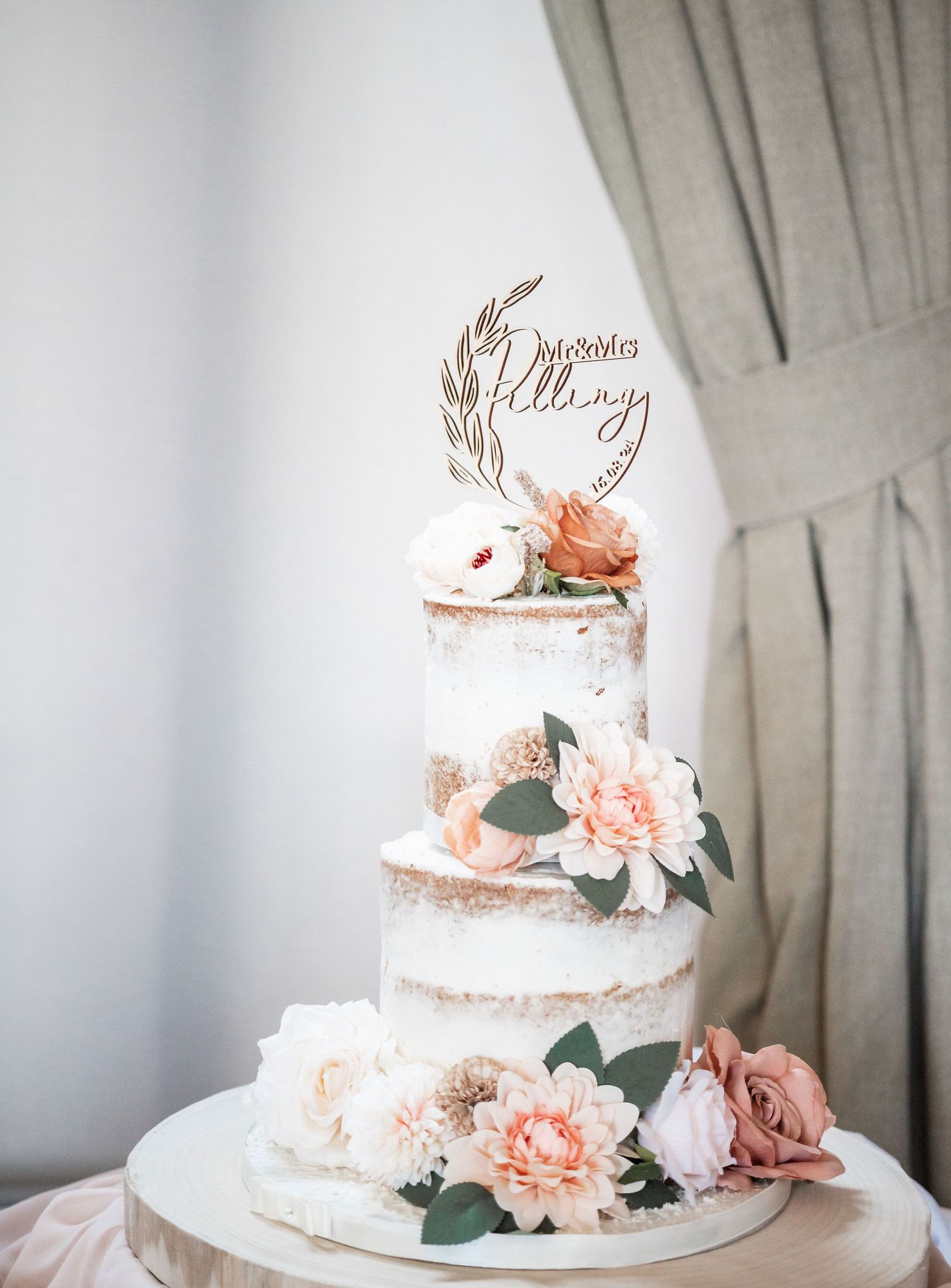 Semi-naked wedding cake decorated with pink flowers and gold wedding topper.