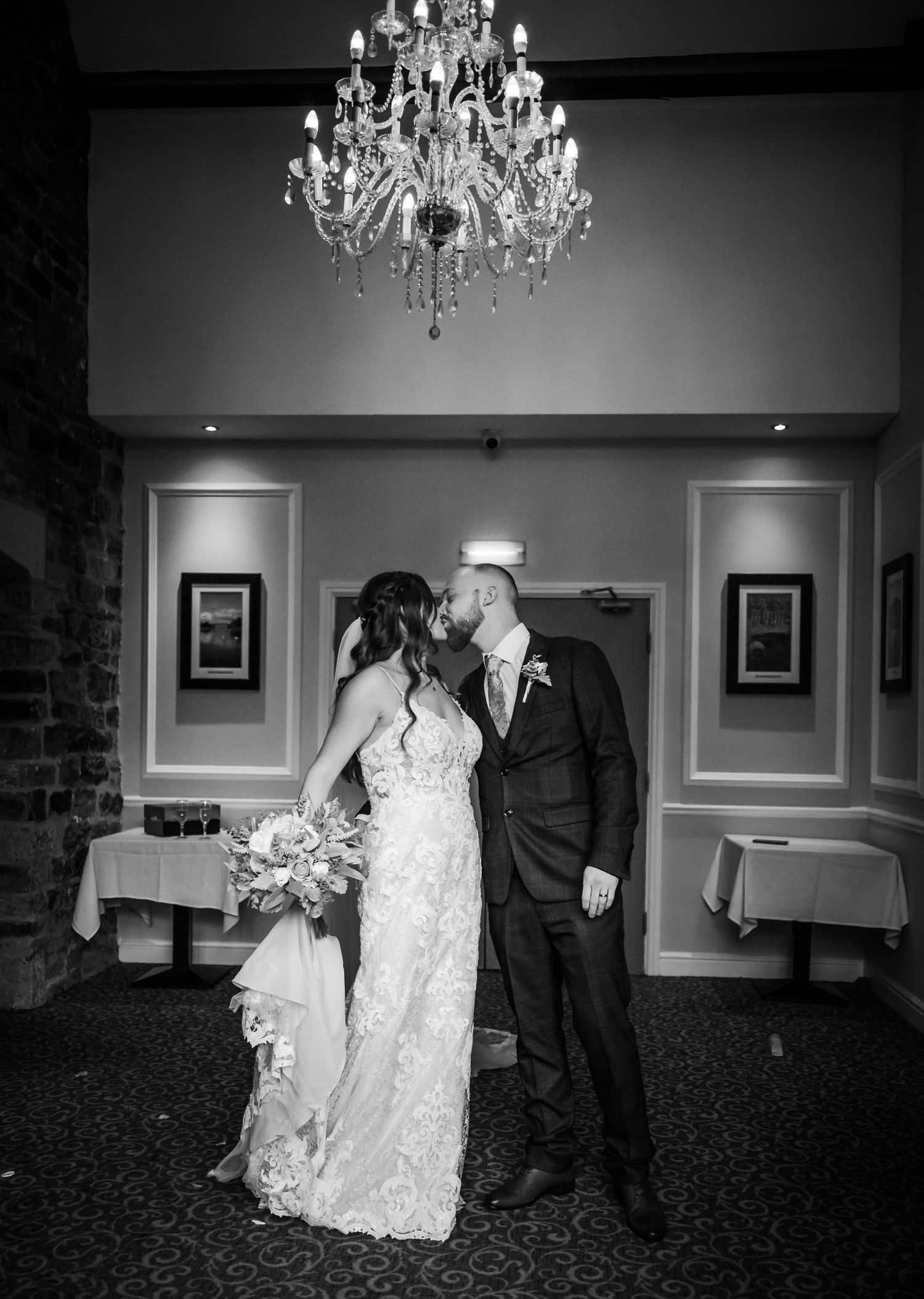 An elegant black and white wedding portrait under a crystal chandelier in a reception venue.