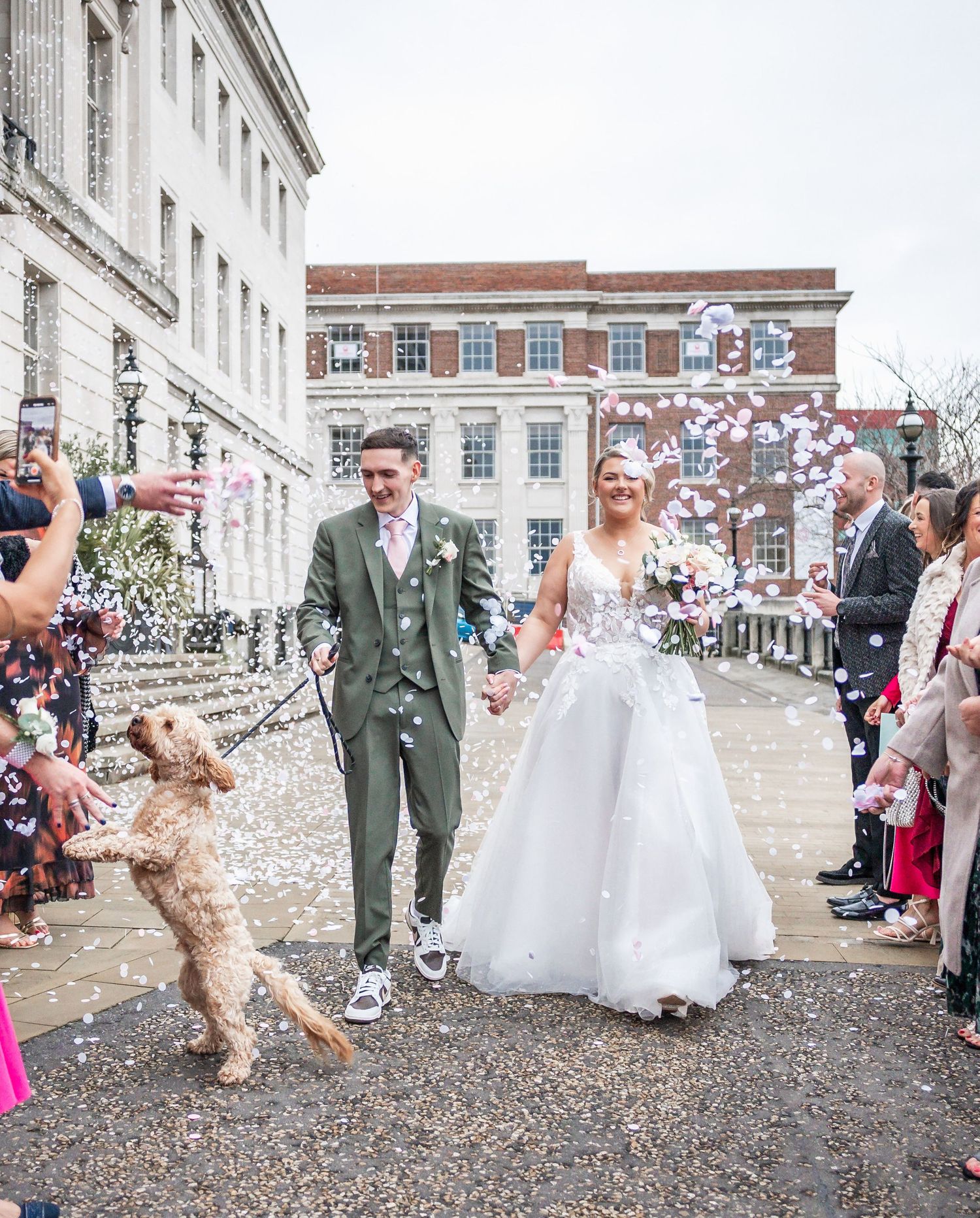 A joyful wedding celebration with confetti flying as a playful dog jumps up during the couple's wedding  exit from Barnsley Town Hall.