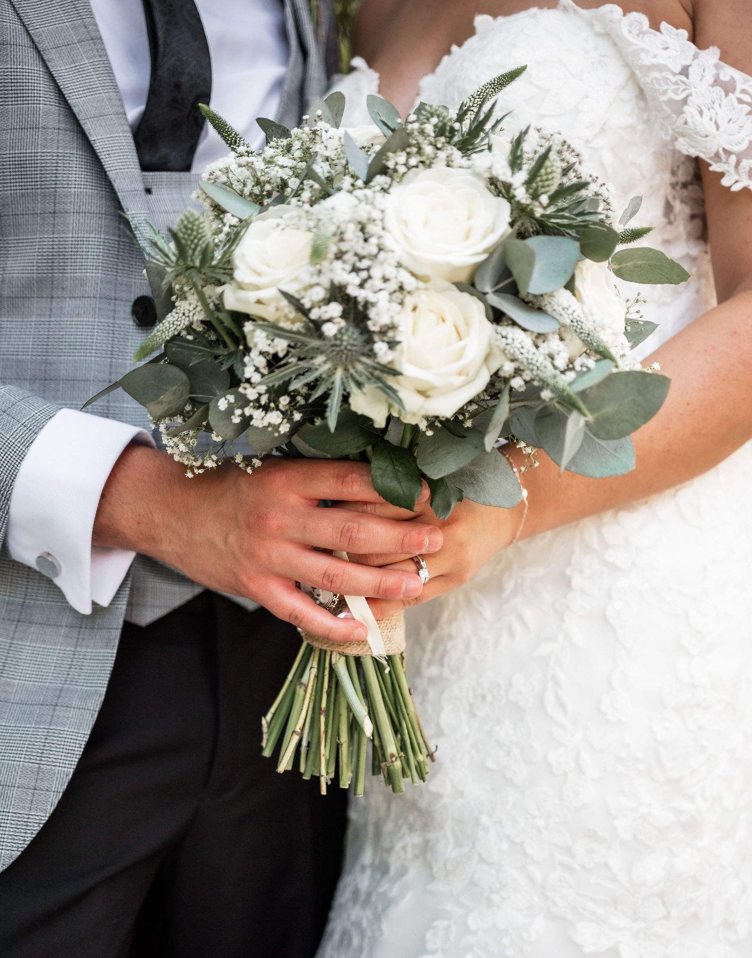 A wedding bouquet featuring white roses, baby's breath and eucalyptus held by newlyweds.