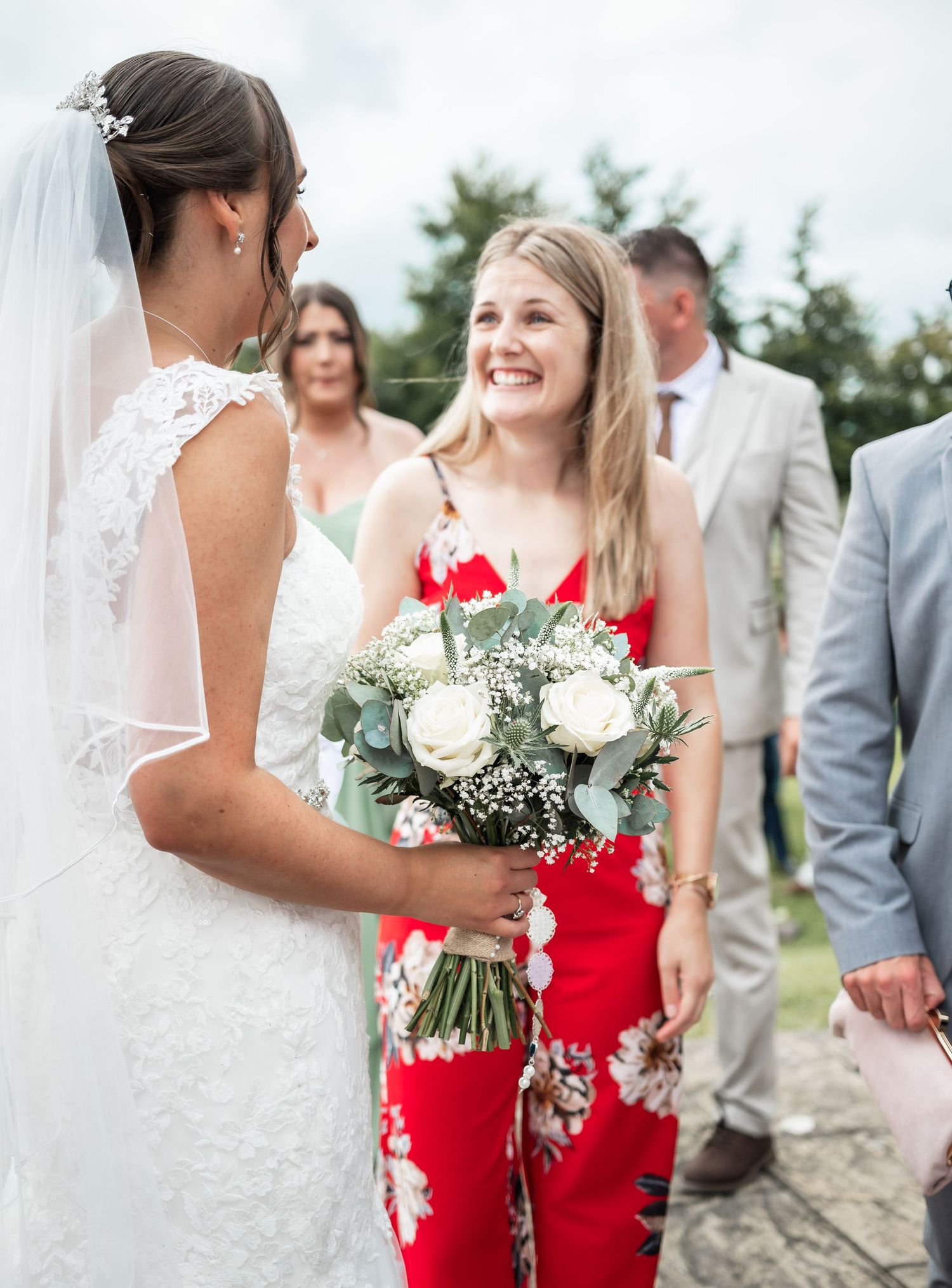 A wedding moment captured outdoors with guests in bright attire and floral bouquets.