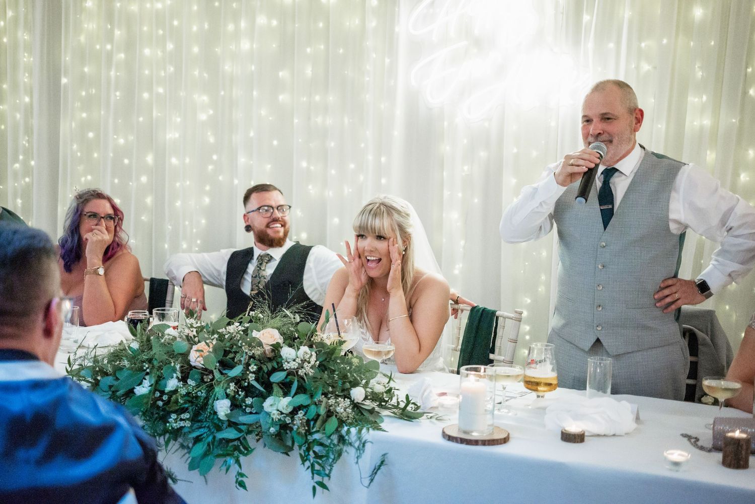 Wedding reception scene with couple at head table decorated with greenery garland.
