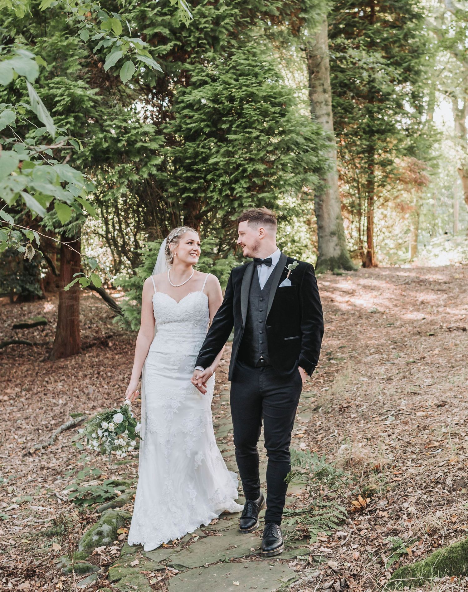 Newlyweds walk hand in hand along a winding forest path during their wedding photoshoot.