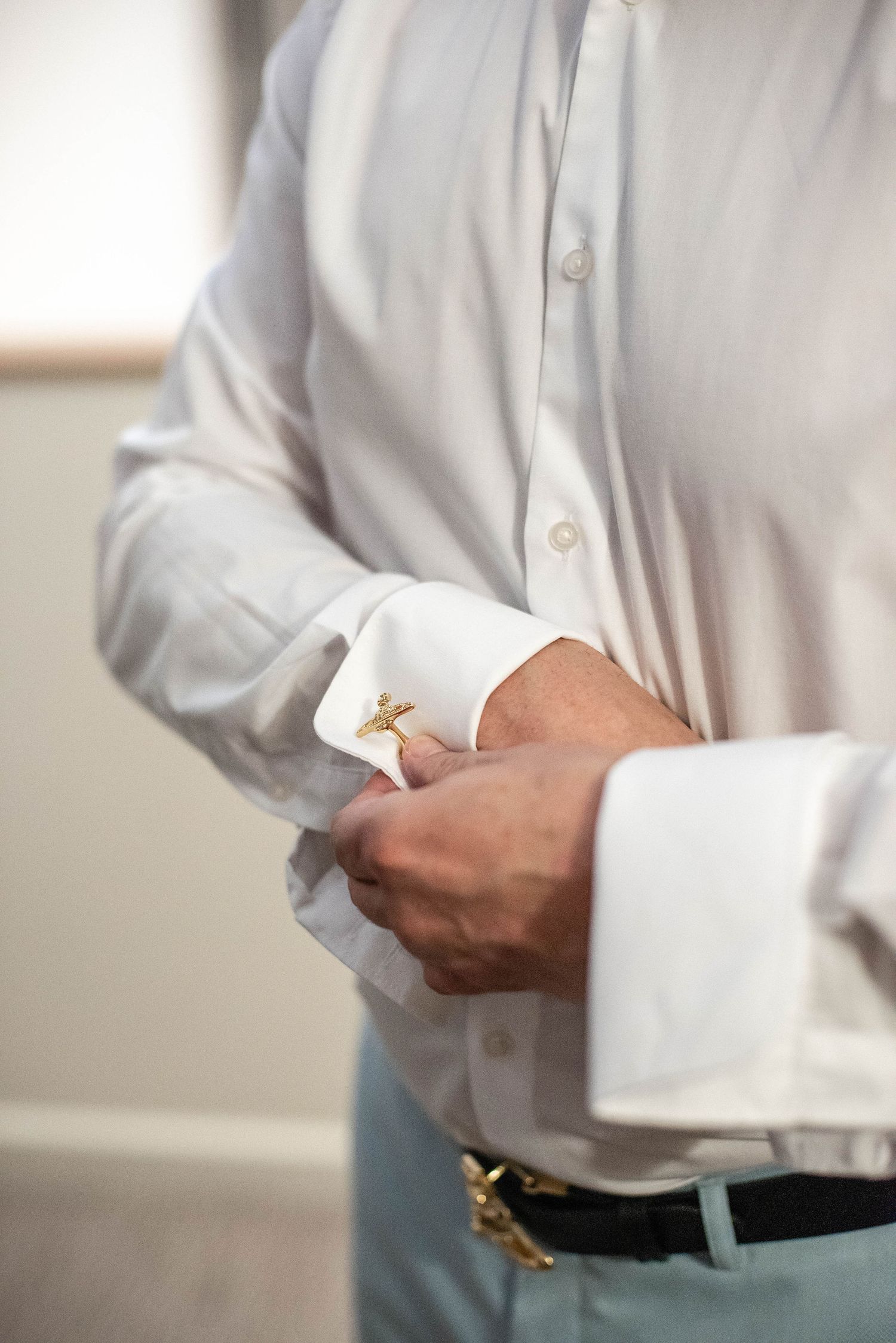Close-up of hands fastening cufflinks on a white dress shirt.