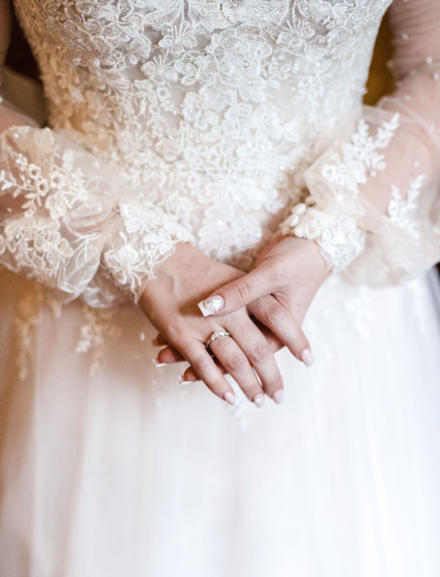 Close up of delicate lace details and wedding ring on bride's hands in white dress.