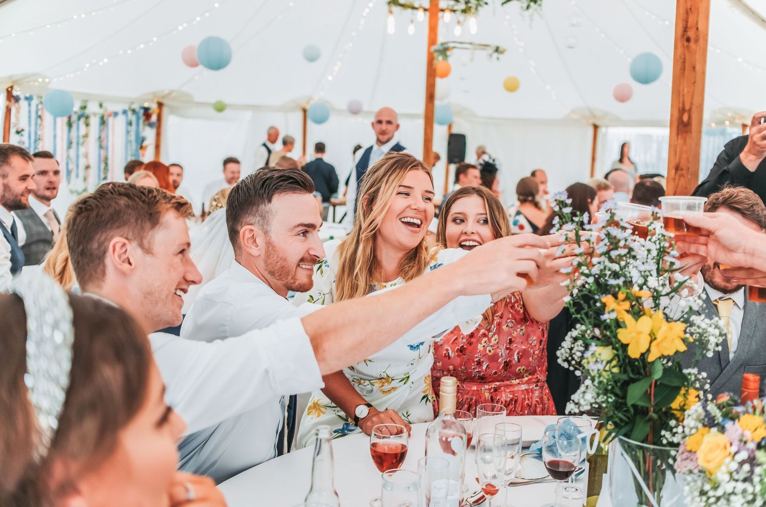 Wedding guests toasting and celebrating at decorated reception table with floral centerpieces.