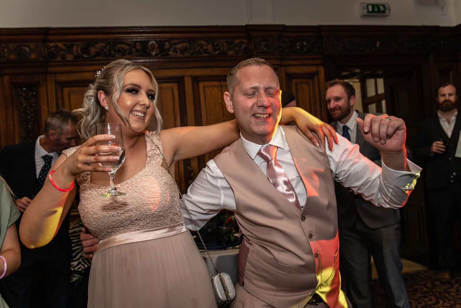 Wedding celebration dancing with guests in formal attire at an ornate indoor reception.