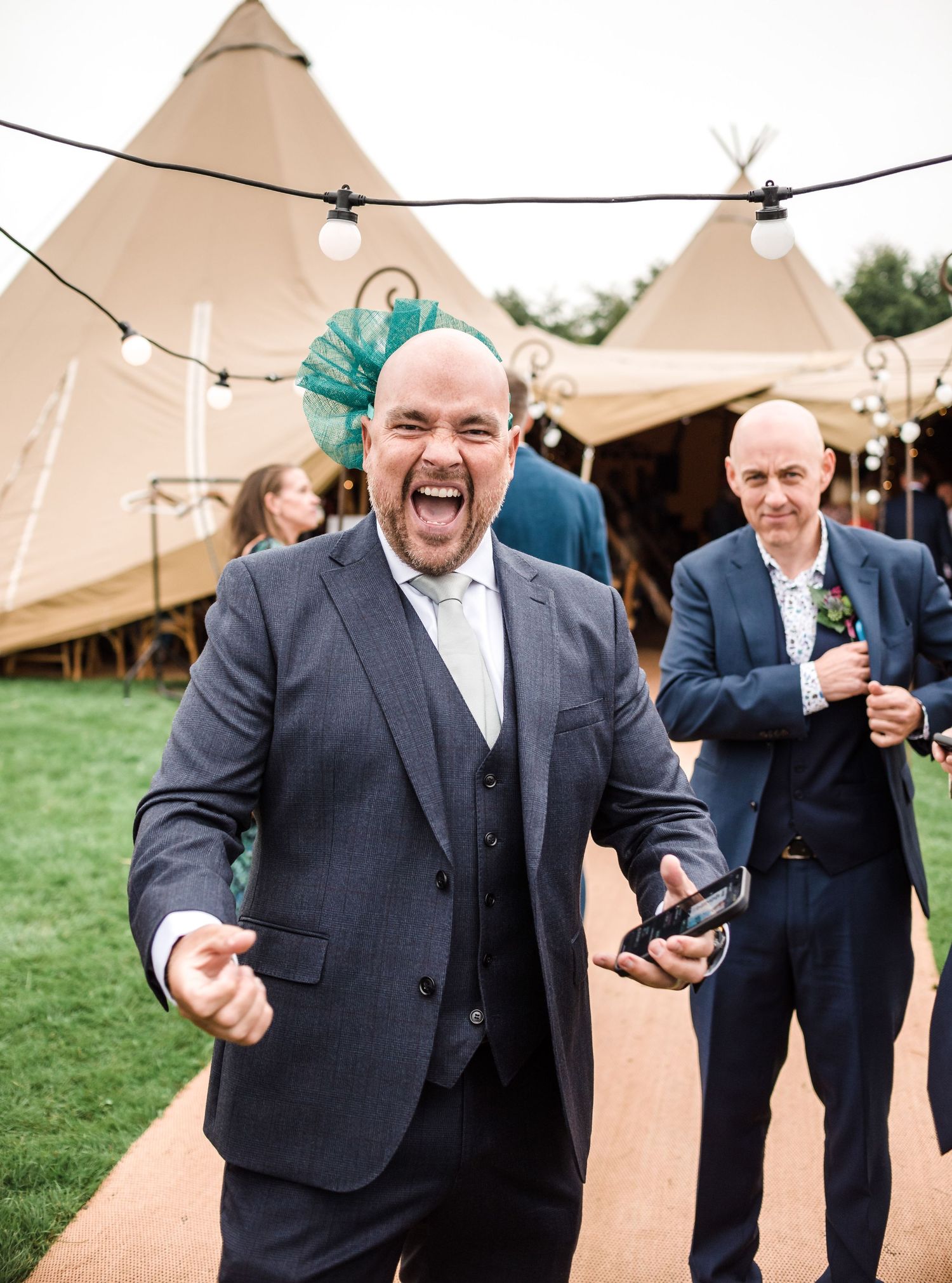 Man in suit with teal bowtie expressing excitement outside tipi tent venue.