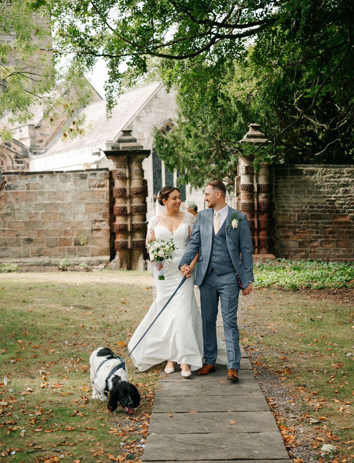 Wedding couple walking along brick pathway surrounded by green gardens.