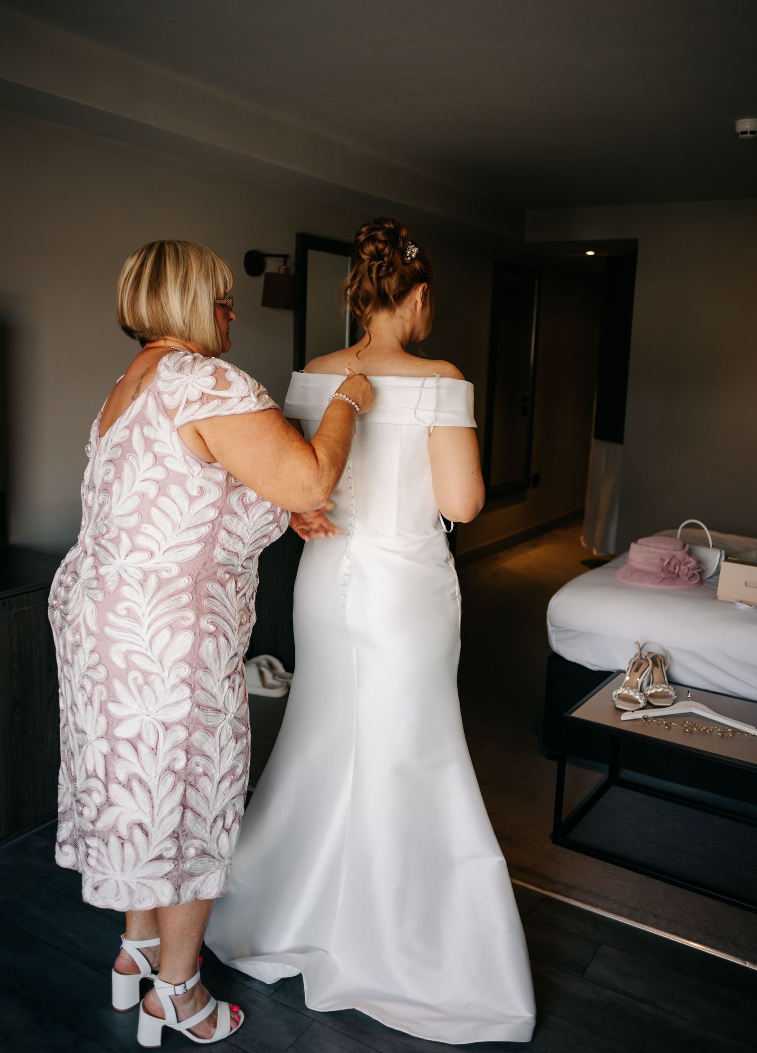 Two people in wedding attire standing together in a dimly lit room with dark flooring.