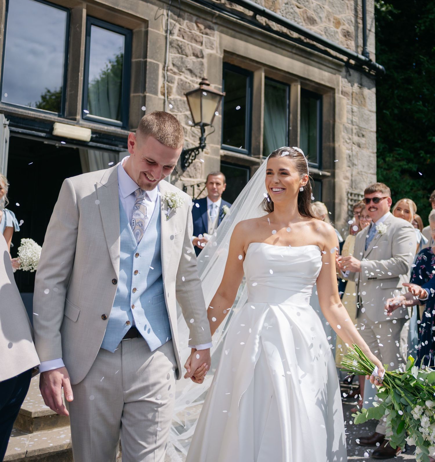 A newlywed couple exits their wedding venue while guests shower them with confetti.