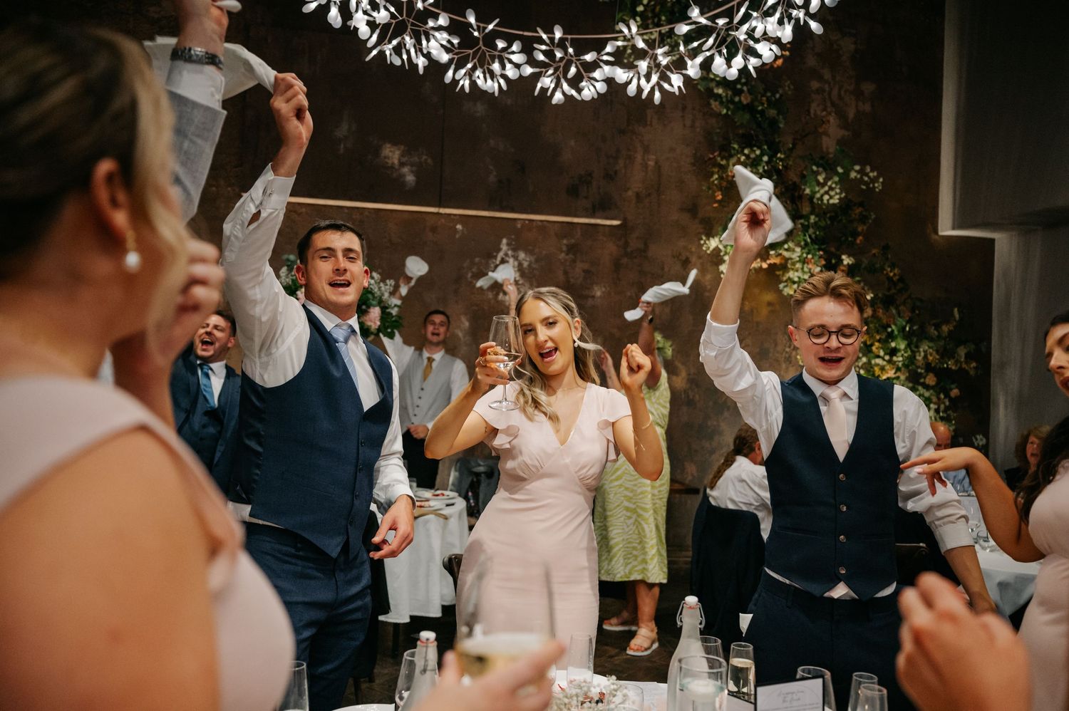 Wedding guests dancing and celebrating together at an indoor reception venue.