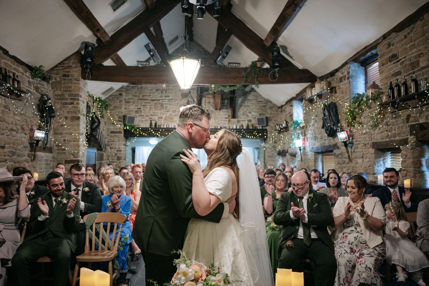Wedding celebration in a rustic stone barn venue with exposed wooden beams and festive decorations.