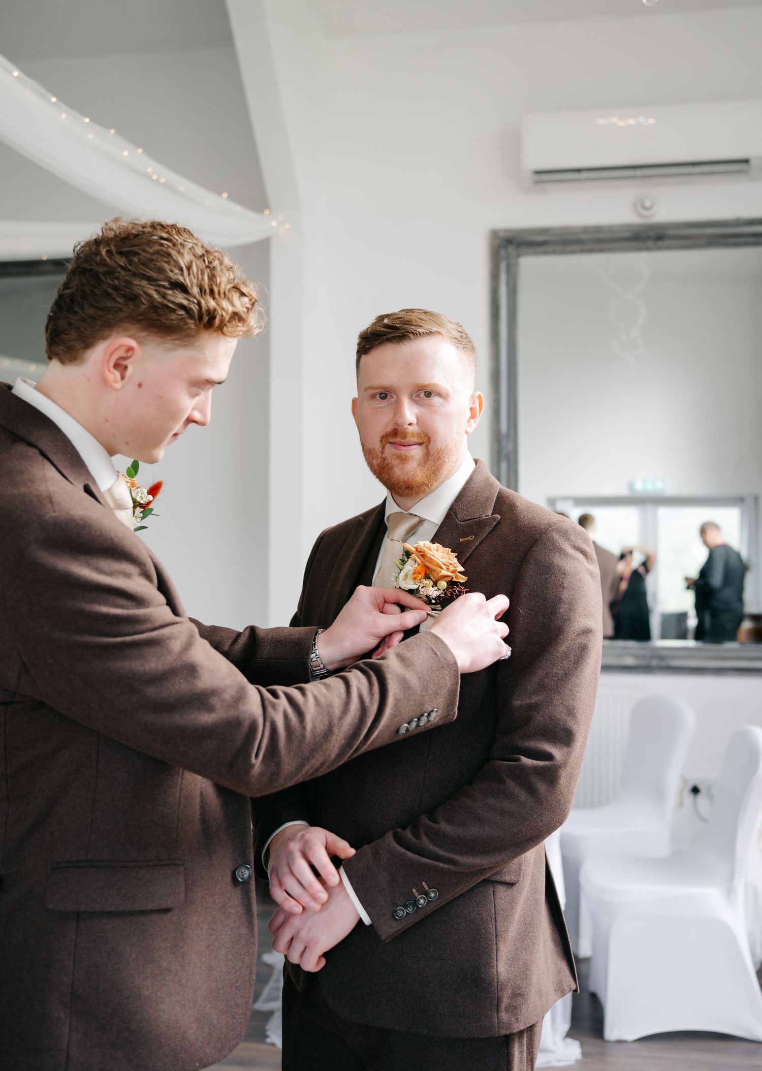 Groomsman helps adjust another's boutonniere before the wedding ceremony.