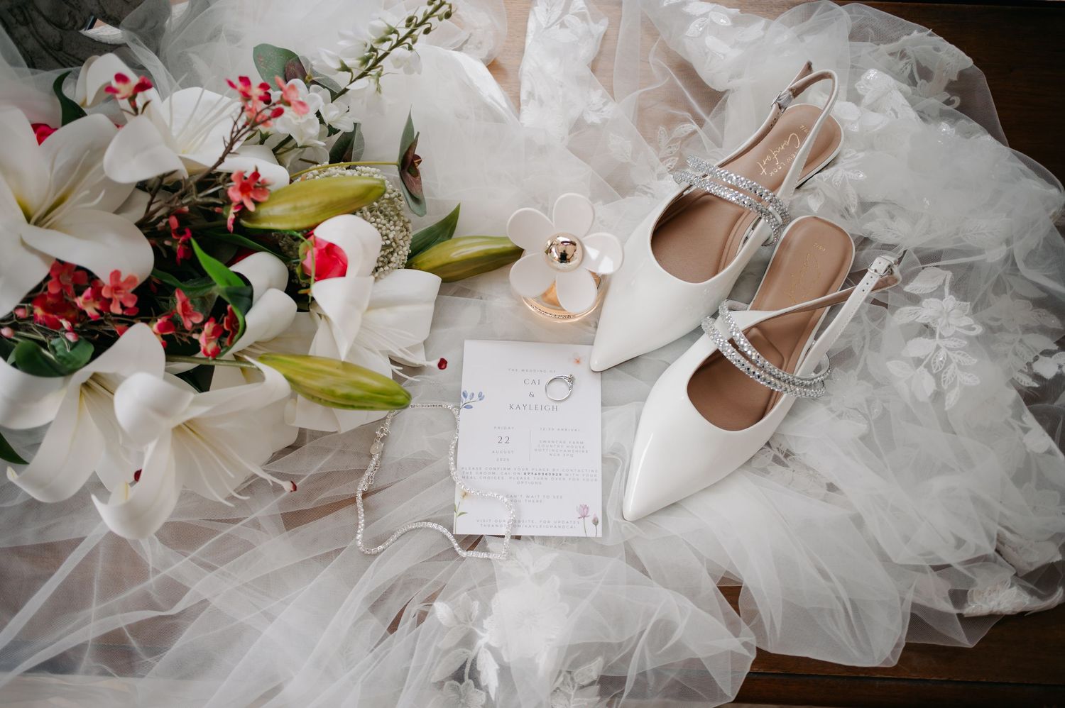 Wedding details showing white bridal gown, elegant shoes, and floral arrangements laid out on a light background.