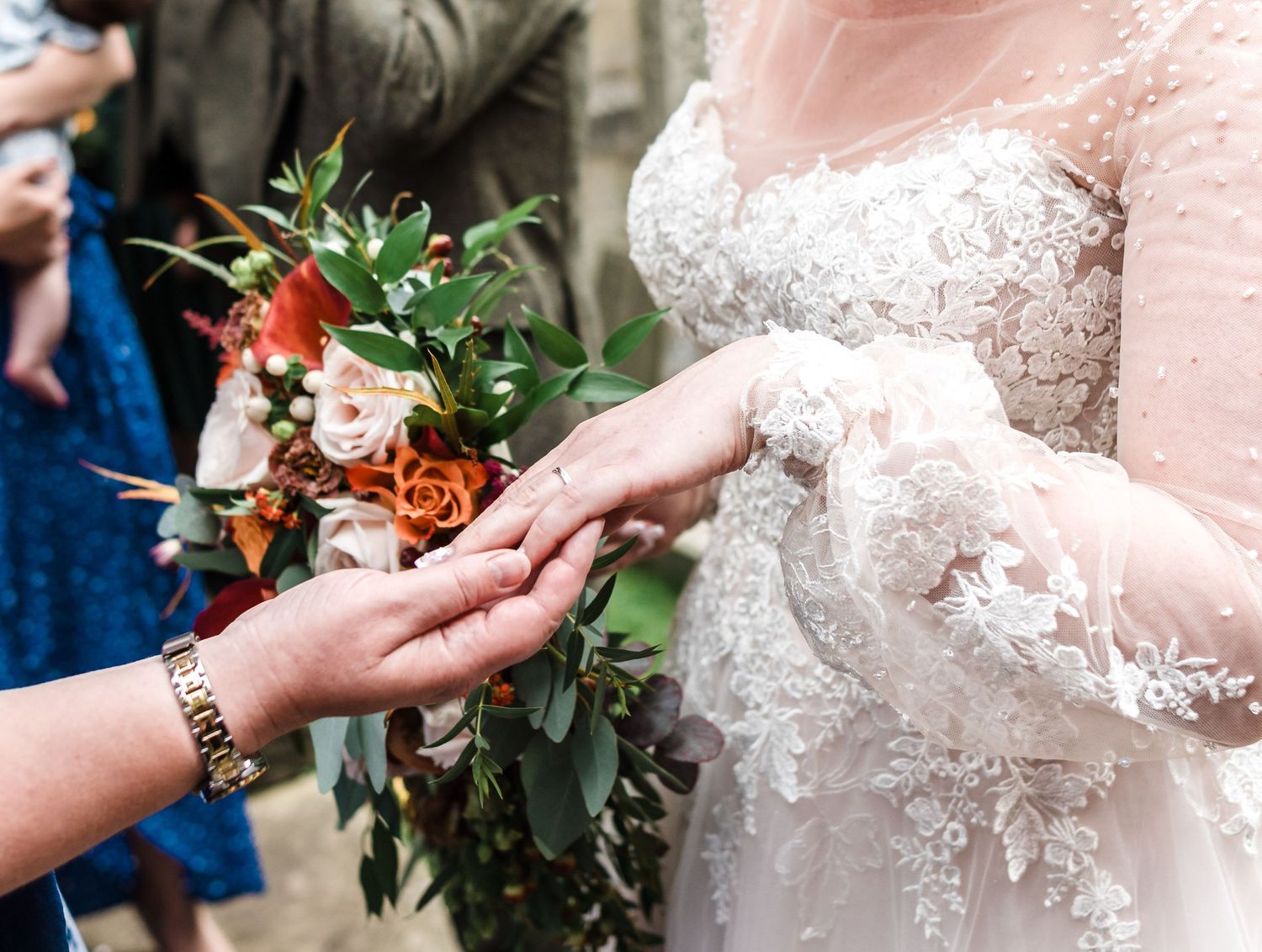 Close-up of wedding bouquet handoff showing lace dress details.