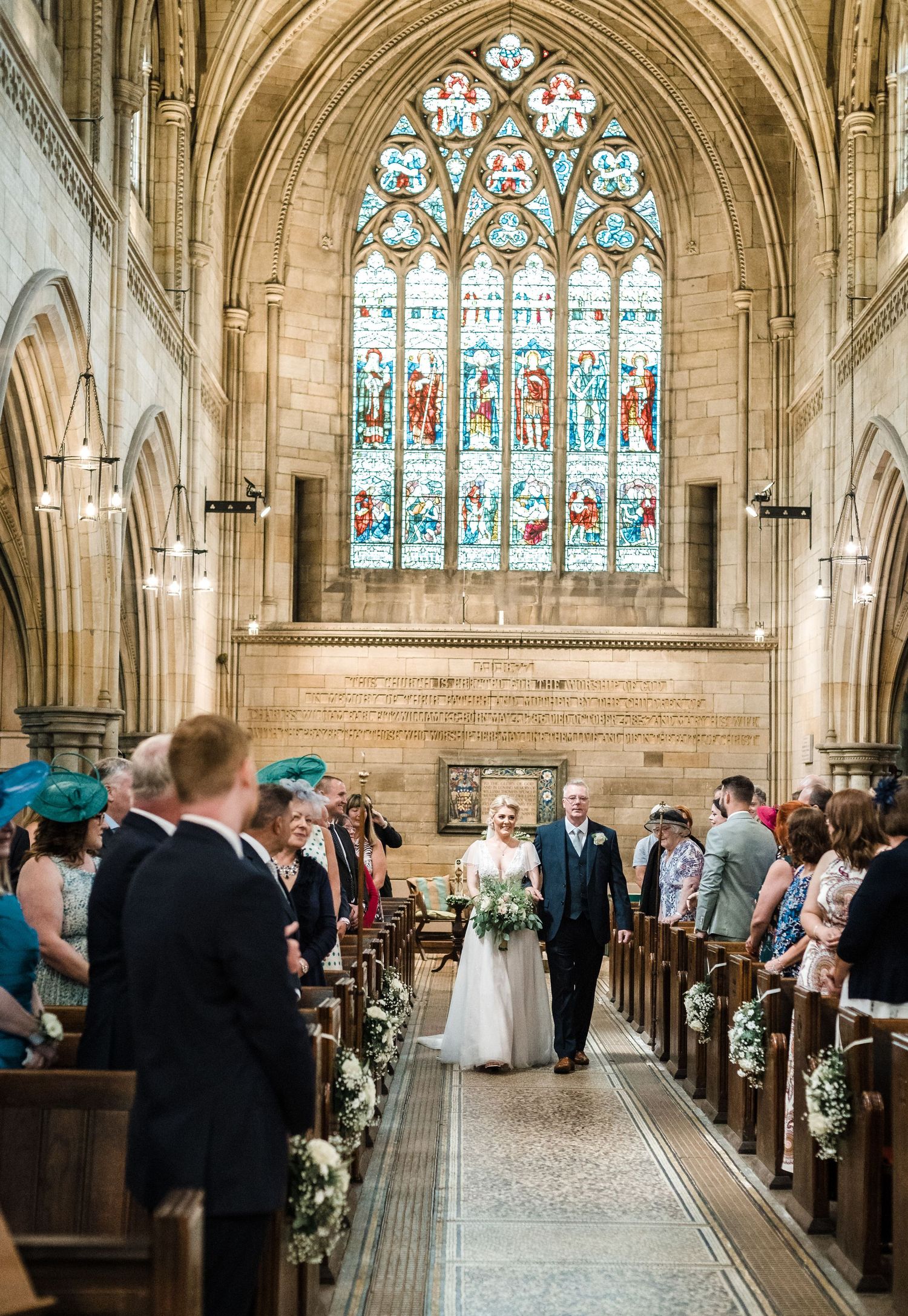 Wedding ceremony procession in a grand cathedral with gothic arches and stained glass windows.