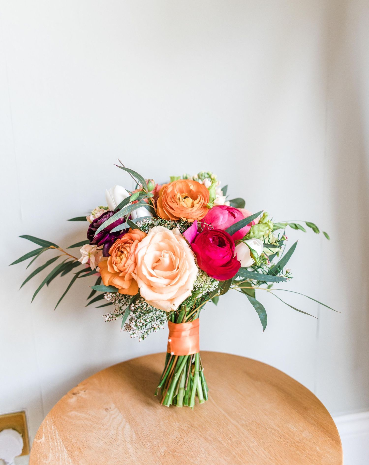 Vibrant bridal bouquet with orange, pink and red roses wrapped in coral ribbon.