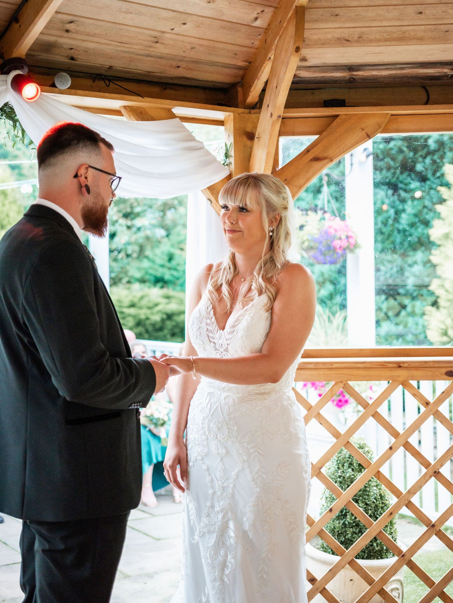 Intimate wedding ceremony moment captured under wooden gazebo with white drapery.