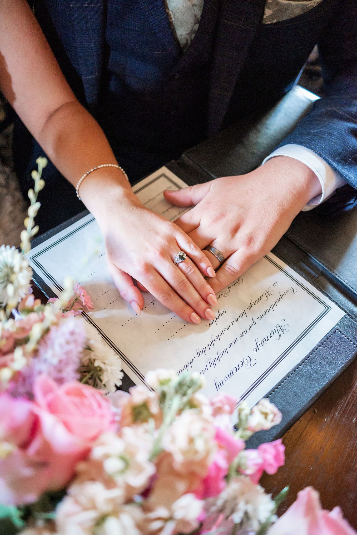 Close-up of hands signing wedding document with pink roses in foreground.