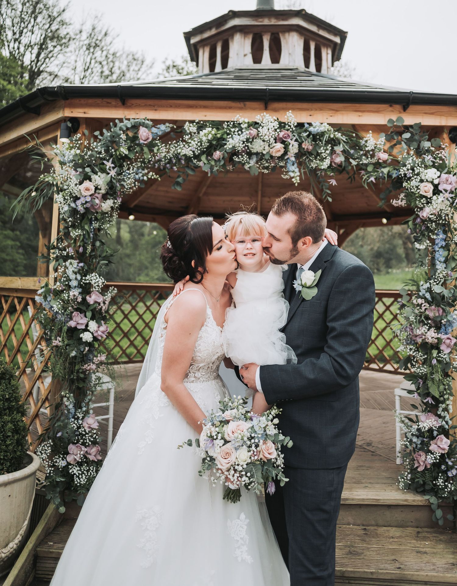Sweet family moment under a floral-decorated gazebo during outdoor wedding ceremony.