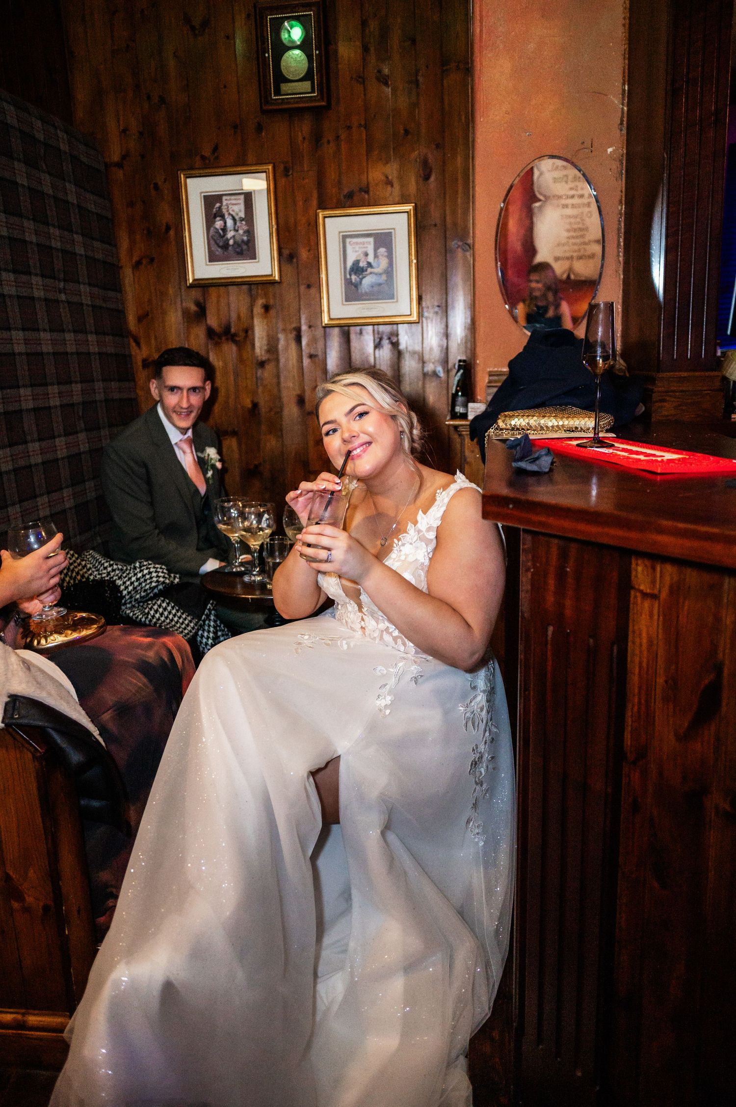 A couple enjoying drinks together at a rustic wooden bar during their wedding celebration.