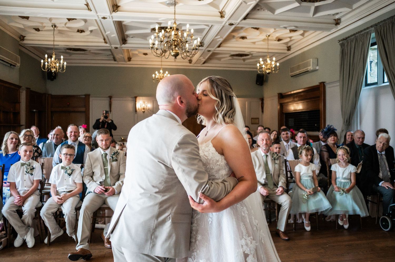 Wedding ceremony in an elegant ballroom with chandeliers and guests seated in rows.