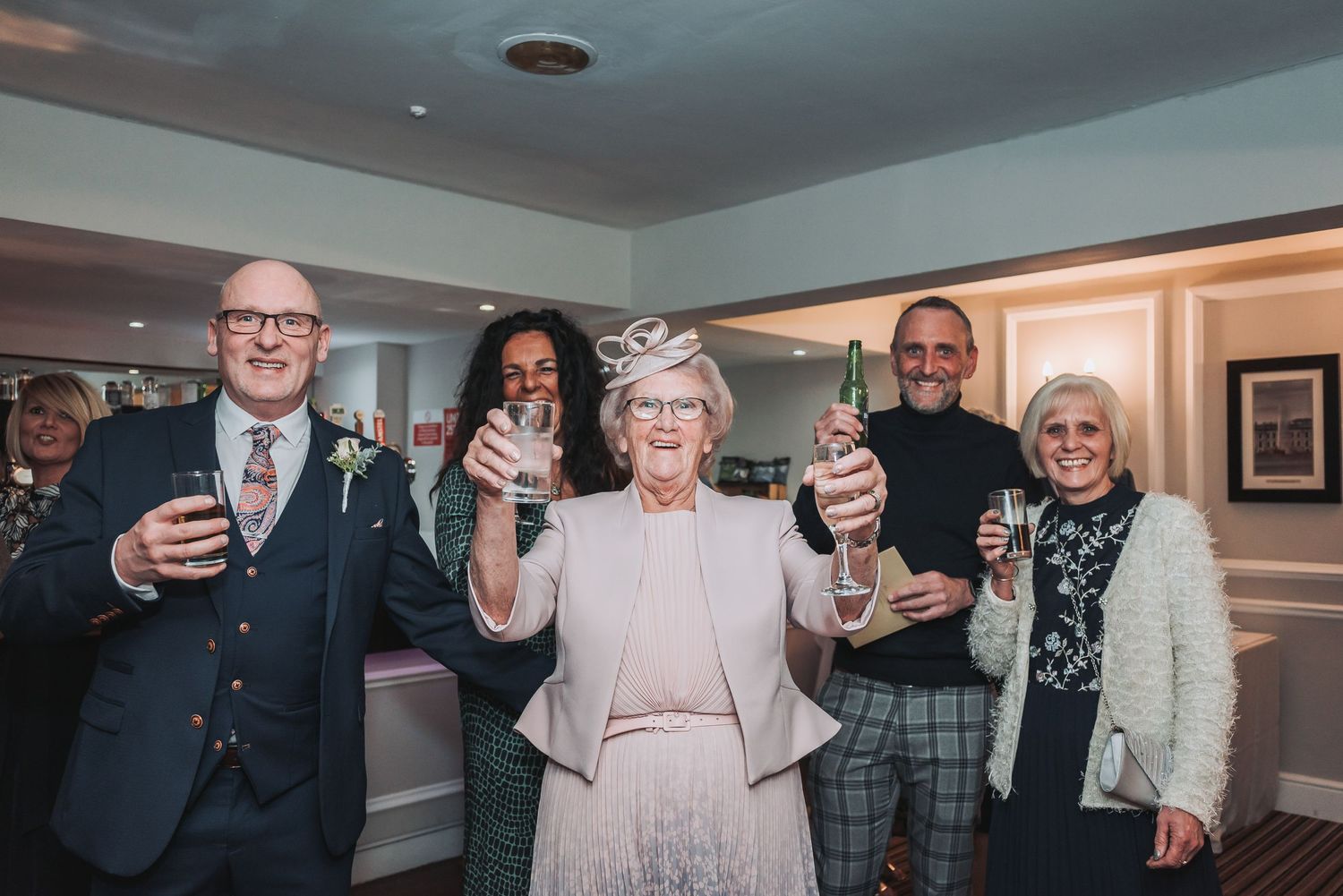 Wedding guests raise their glasses in celebration at an indoor reception venue.