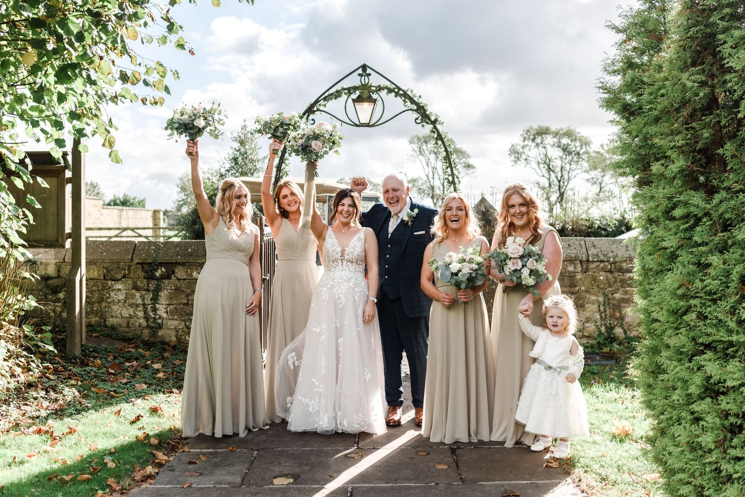 Wedding party posing under a floral arch in a garden setting.