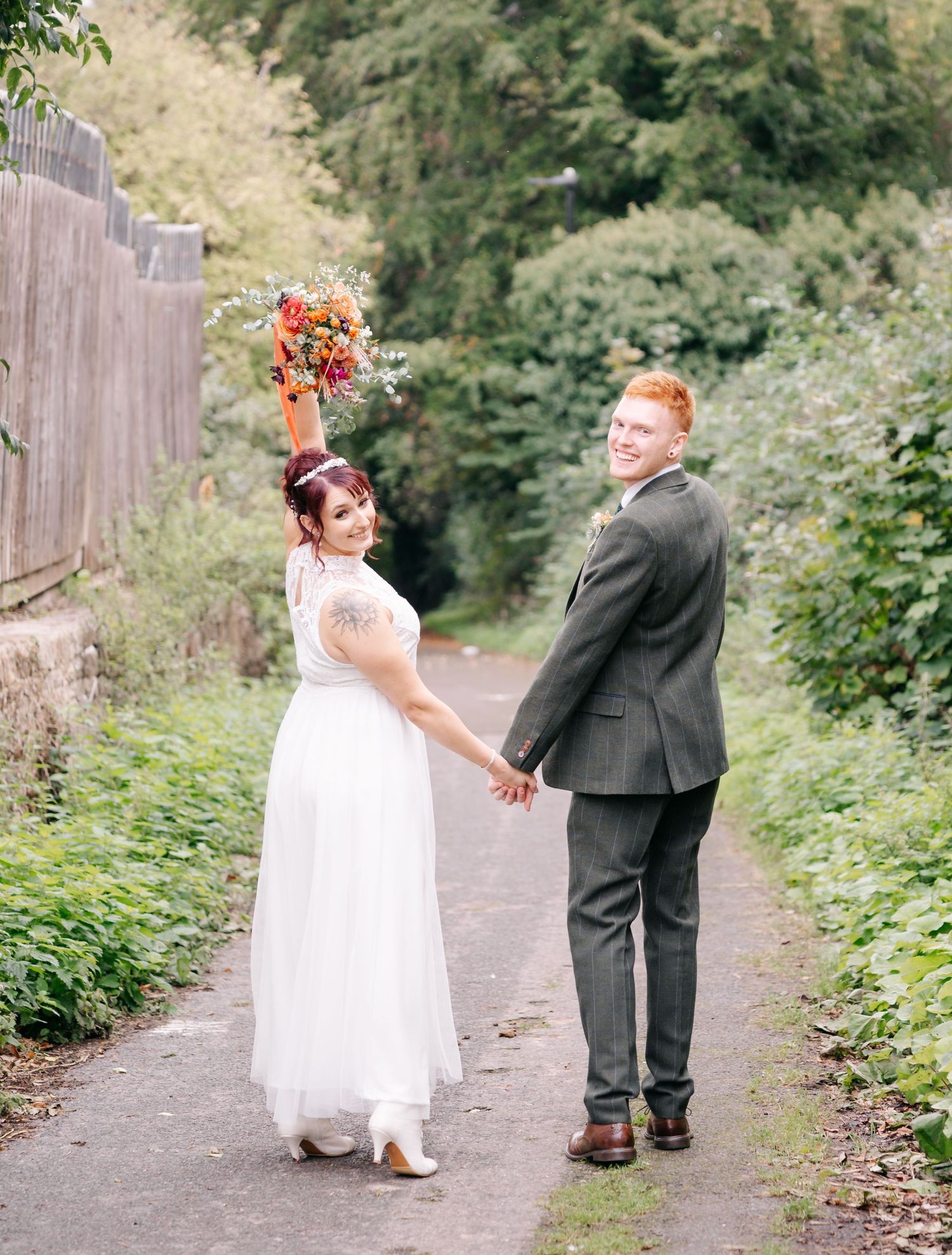 Newlyweds walking on a garden path with the bride holding up a vibrant autumn bouquet.