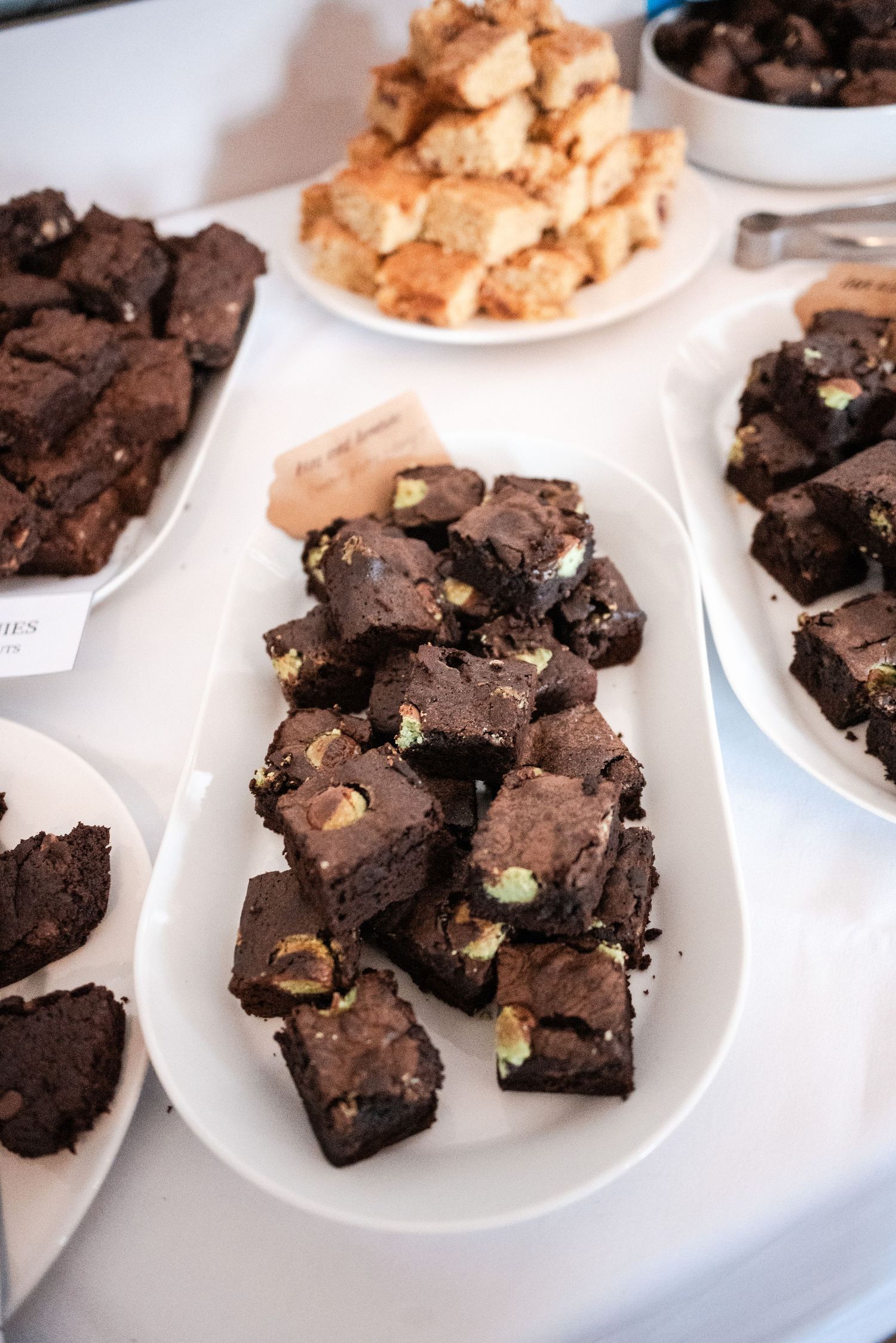 Plates of chocolate brownies and other desserts displayed on a white table.