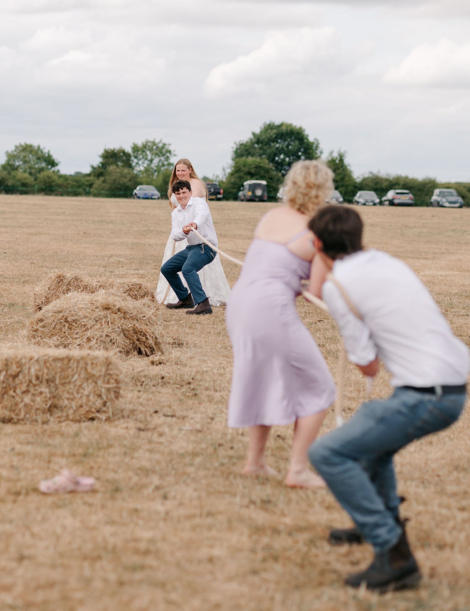 Playful wedding party members roll down grassy hill during outdoor photo session.