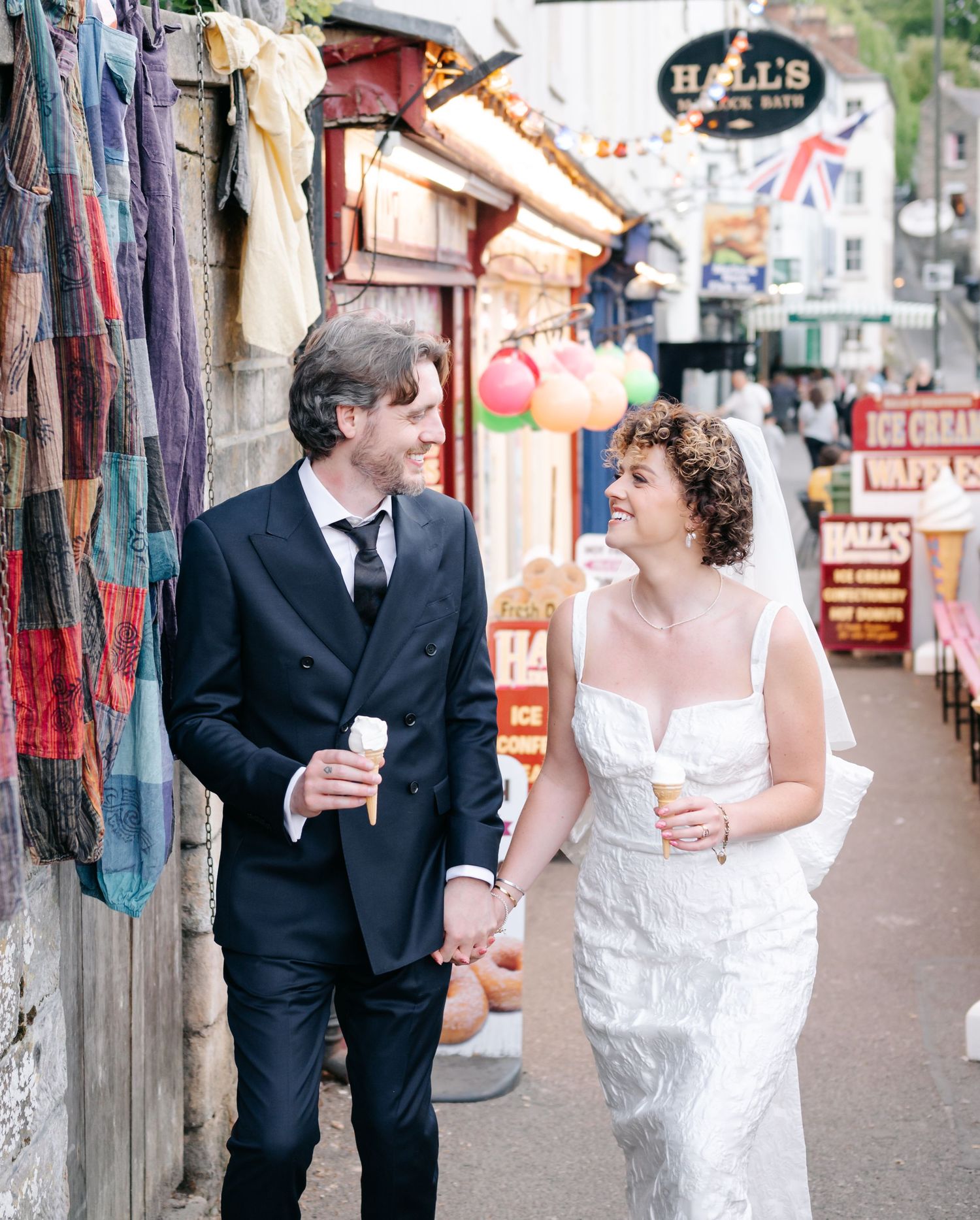 A couple walks hand in hand past colorful market stalls during their wedding photo session.