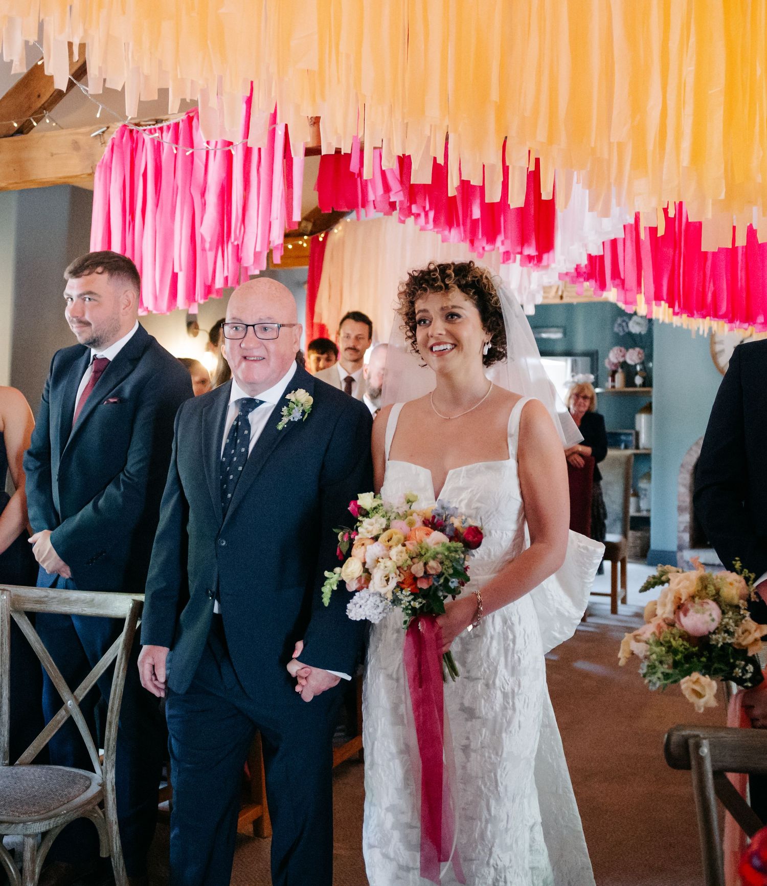 Wedding ceremony setup with pink and peach streamers hanging from the ceiling in an indoor venue.